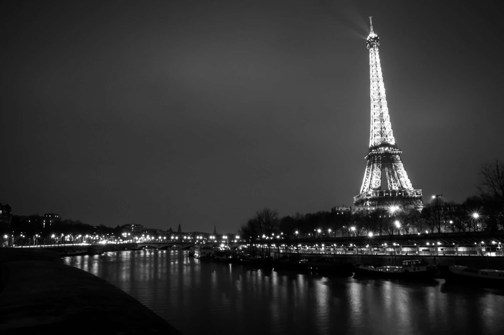 Paris At Night 桌布 壁紙 — 艾菲爾鐵塔在夜晚閃耀光芒，其燈光倒映在下面的塞納河上，形成引人注目的黑白構圖。