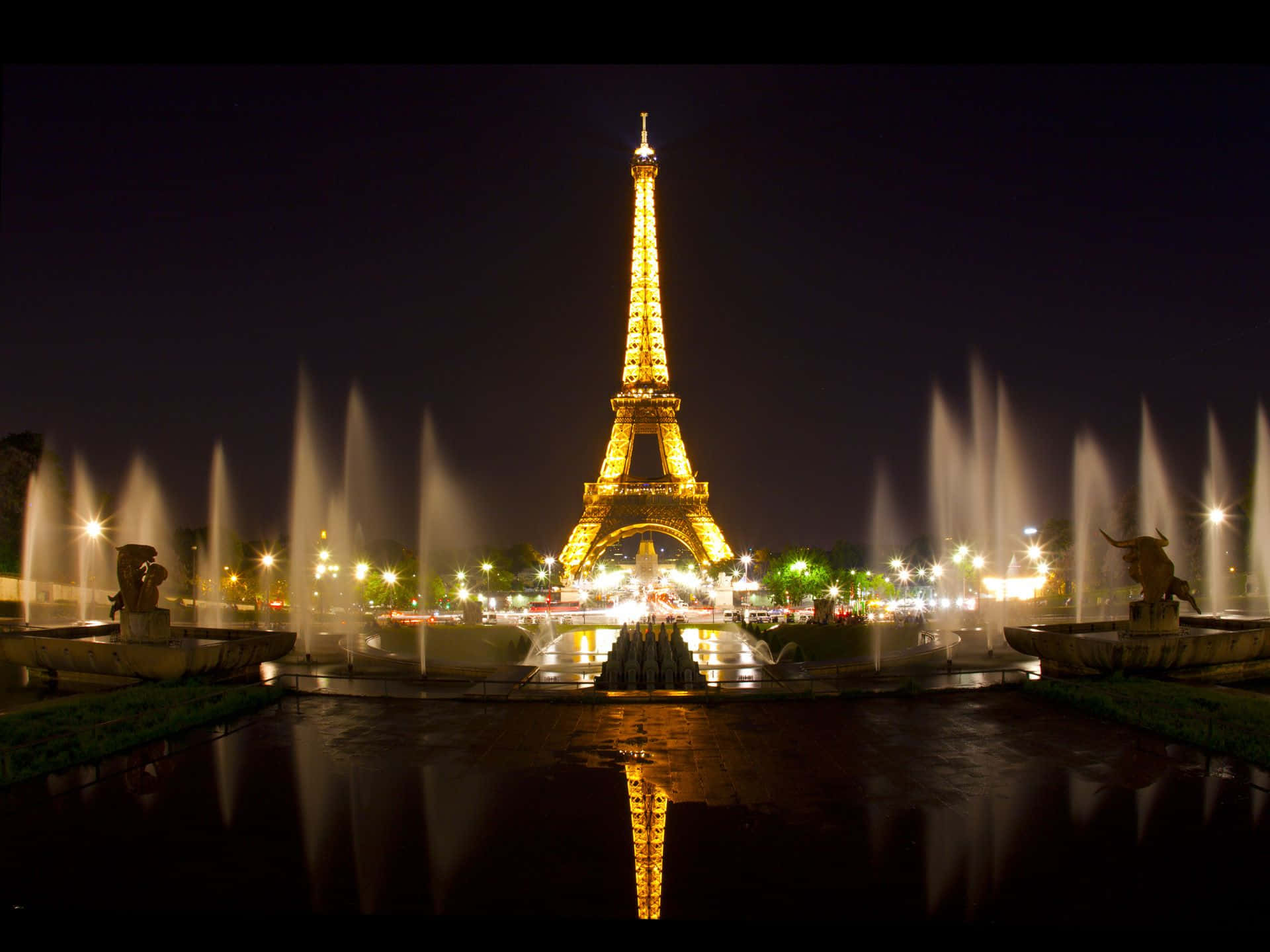 Eiffel Tower 桌布 壁紙 — 艾菲爾鐵塔在夜晚閃耀金色光芒，倒映在噴水池中，水柱在黑暗天空下對稱拱起。