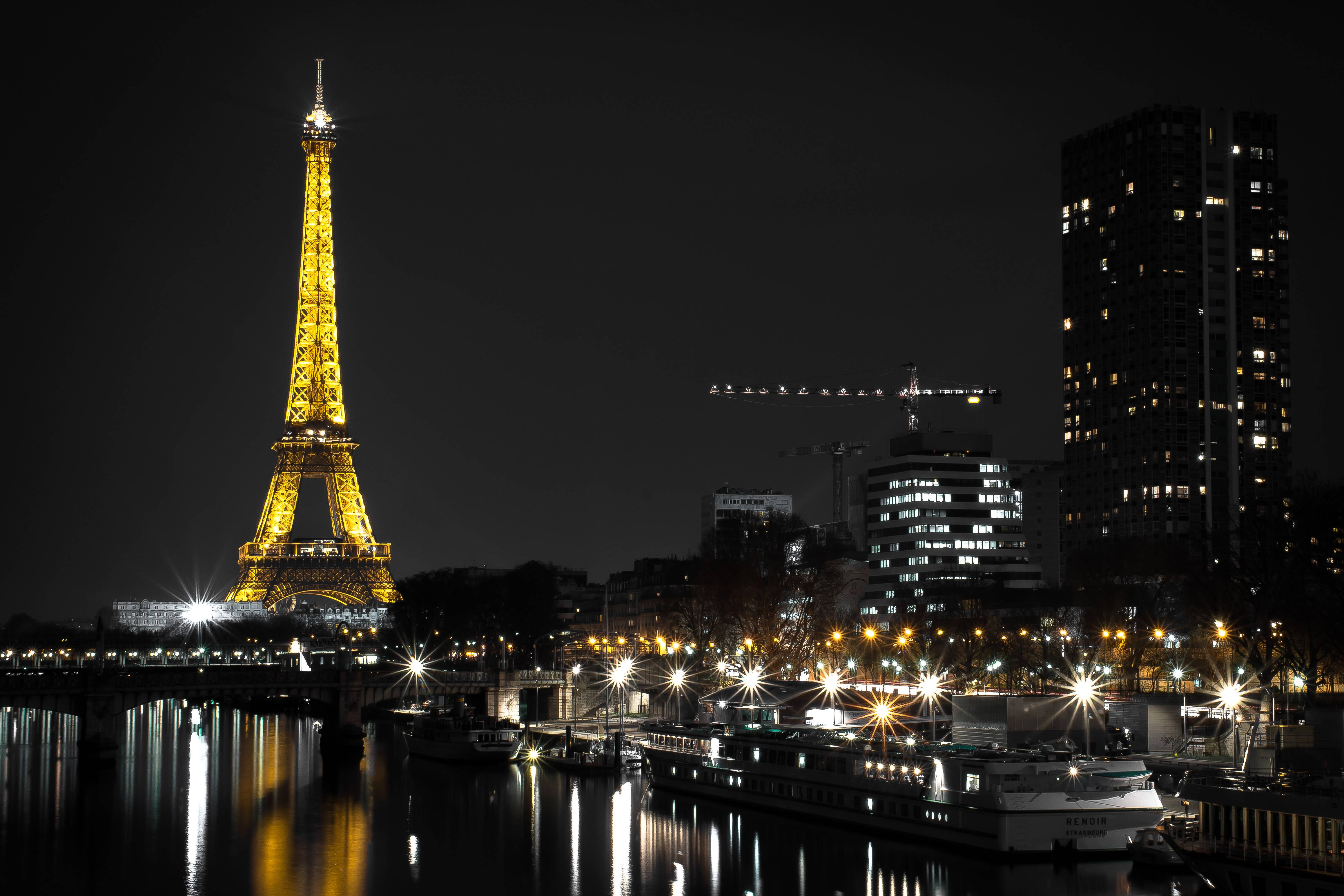 France 桌布 壁紙 — 艾菲爾鐵塔在夜空中閃耀著金色光芒，燈光倒映在塞納河上，附近的船隻和城市建築也閃閃發光。
