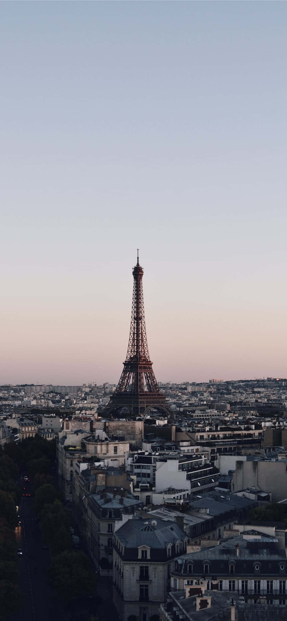 Paris Aesthetic 桌布 壁紙 — 艾菲爾鐵塔在巴黎屋頂上方升起，在柔和的暮色天空下呈現粉彩粉紅和藍色調。