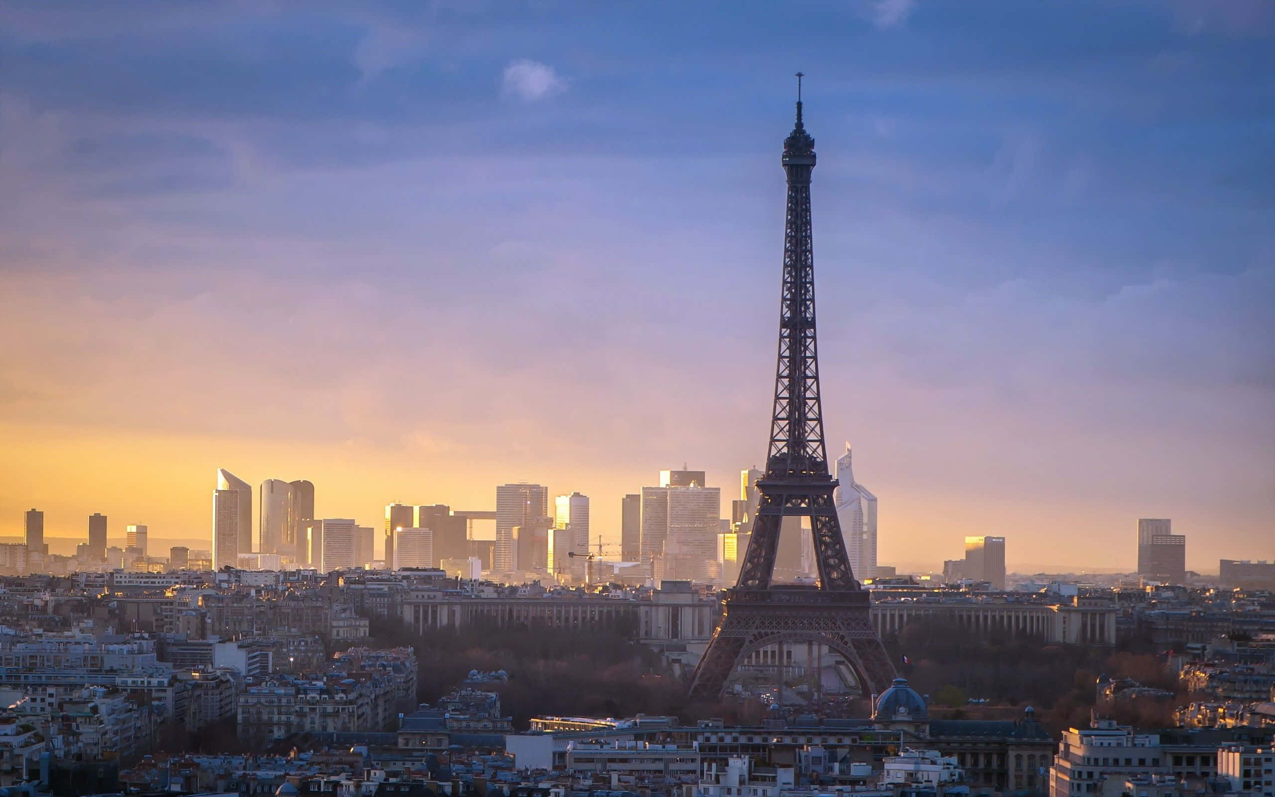 Paris Desktop 桌布 壁紙 — 艾菲爾鐵塔在巴黎屋頂和現代摩天大樓之上，聳立在金色的日落天空下。