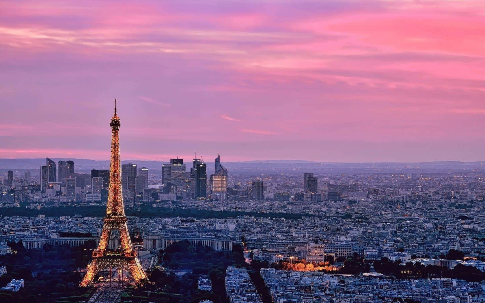 Paris Eiffel Tower 桌布 壁紙 — 艾菲爾鐵塔在巴黎屋頂和現代摩天大樓上空的夢幻粉紫色暮色天空中閃耀著金色光芒。
