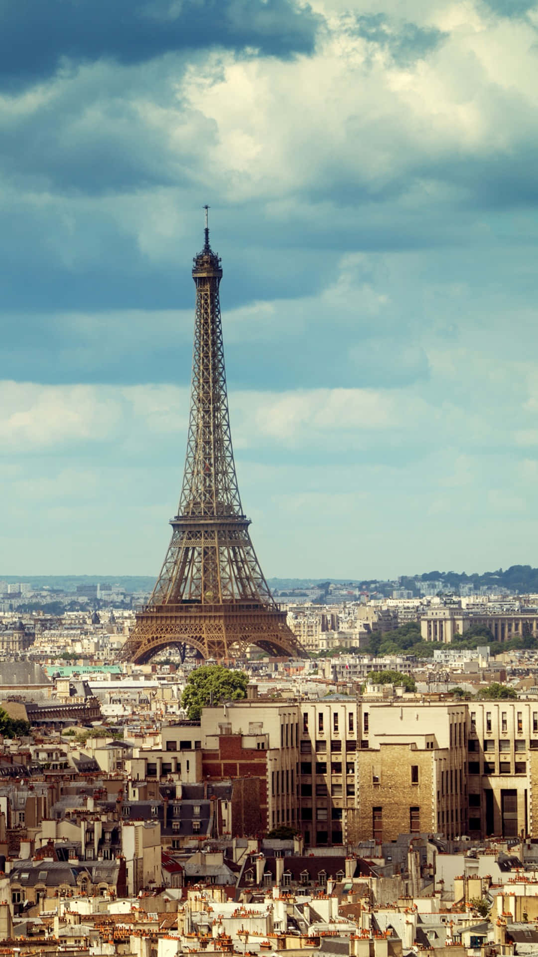 Paris Eiffel Tower 桌布 壁紙 — 艾菲爾鐵塔在戲劇性的多雲天空下，雄偉地聳立在巴黎屋頂之上。