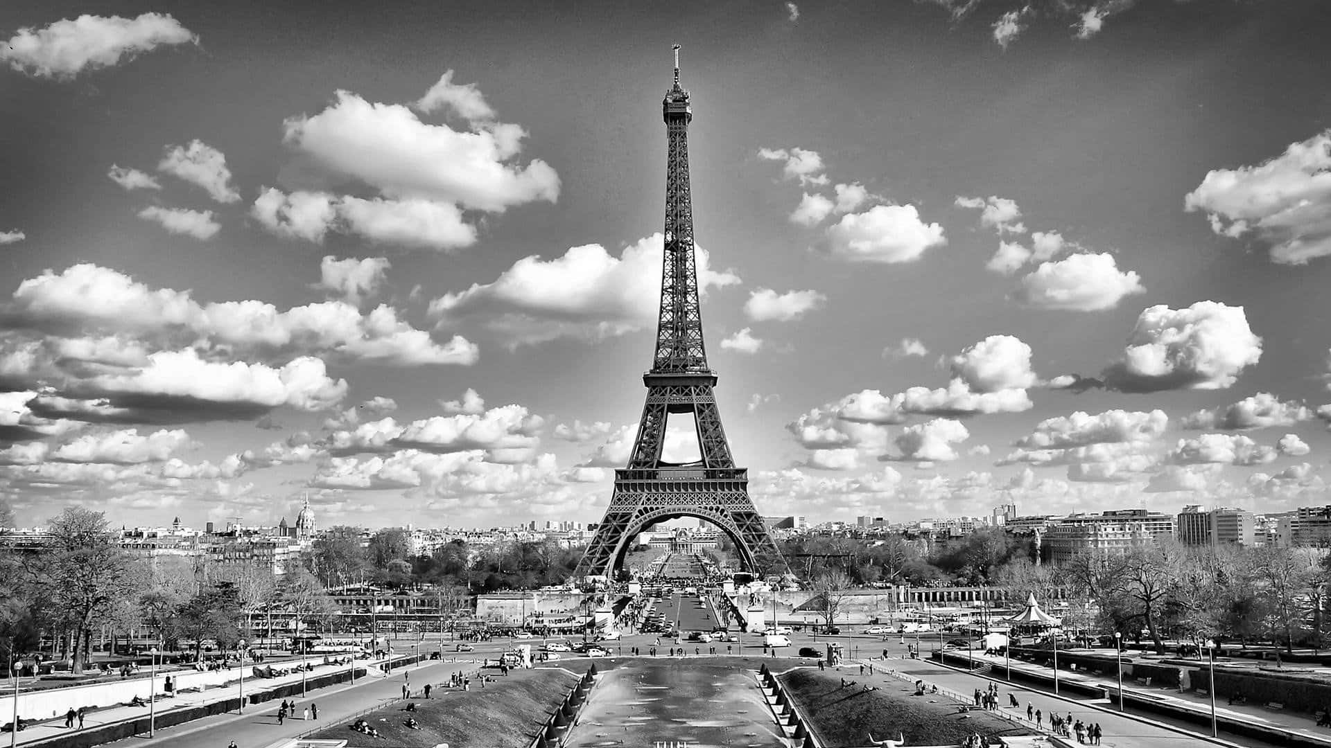 Paris Aesthetic 桌布 壁紙 — 艾菲爾鐵塔在戲劇性的天空下，散雲和下方繁忙小徑的黑白景觀。