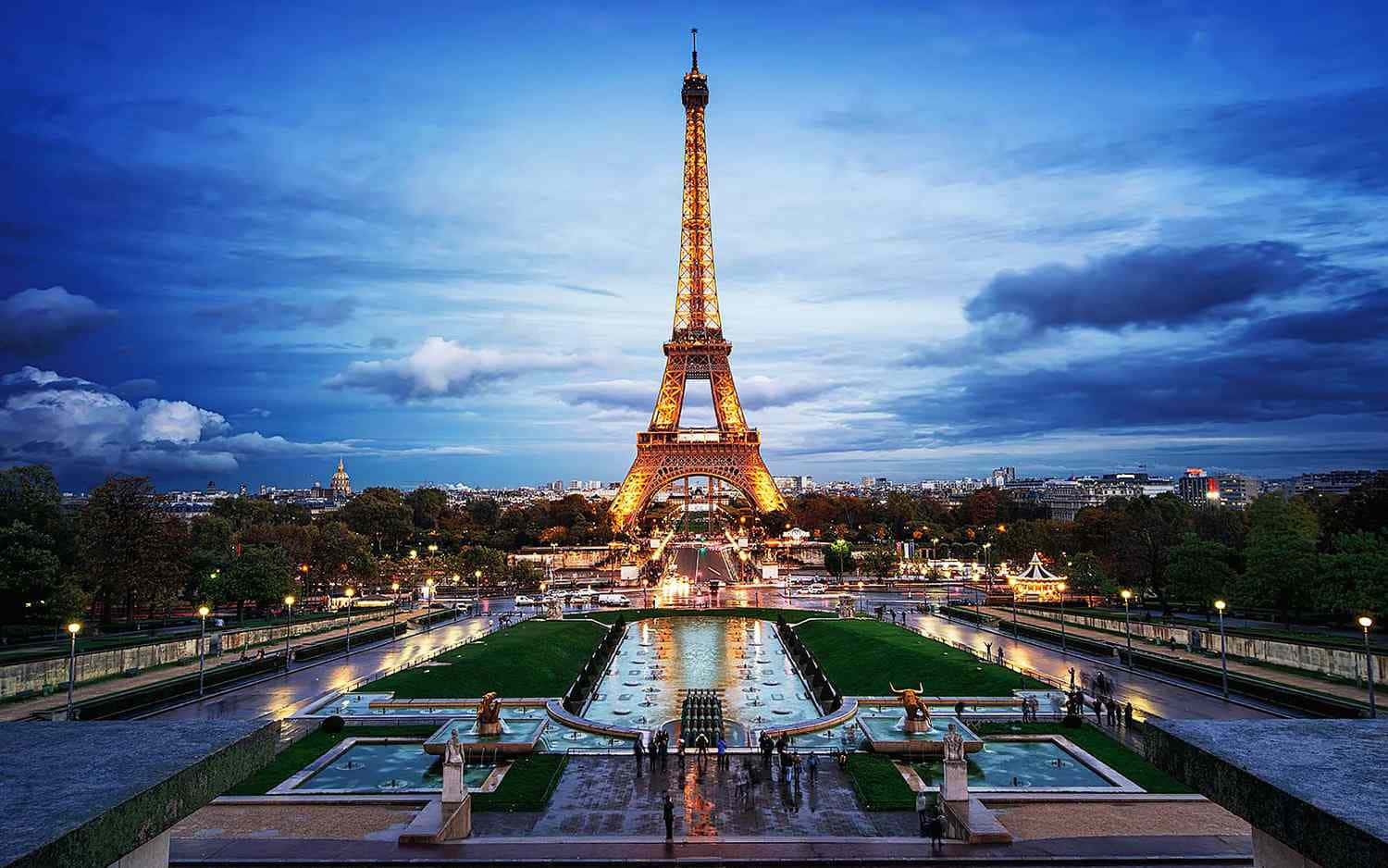 France 桌布 壁紙 — 艾菲爾鐵塔在戲劇性的暮色天空中溫暖地發光，燈光倒映在下方宏偉的噴泉中。