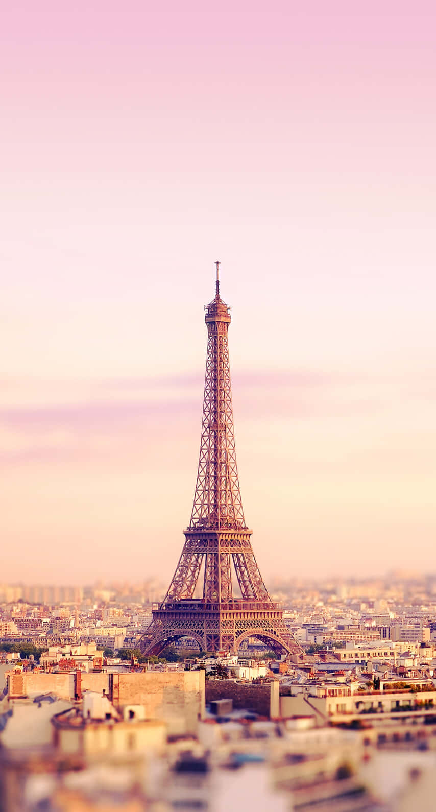 Paris Aesthetic 桌布 壁紙 — 艾菲爾鐵塔在日落時分聳立在柔和的粉紅色和蜜桃色天空下，背景是模糊的巴黎城市景觀。