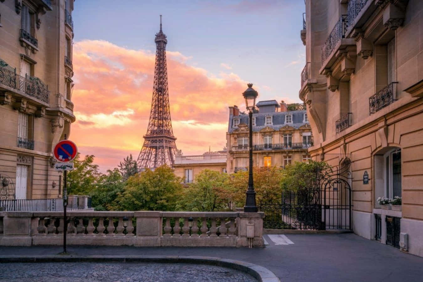 France 桌布 壁紙 — 艾菲爾鐵塔在日落時分雄偉地聳立在巴黎屋頂之上，將溫暖的金色光芒灑在歷史建築和鵝卵石街道上。