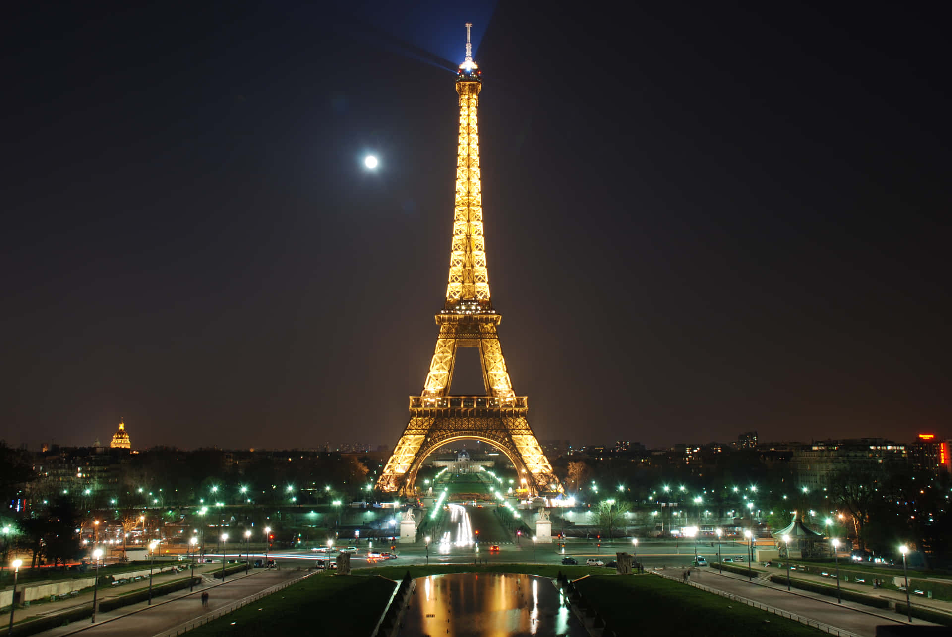 Eiffel Tower 桌布 壁紙 — 艾菲爾鐵塔在明亮的月光夜空下溫暖地發光，前景的水面反射著城市燈光。