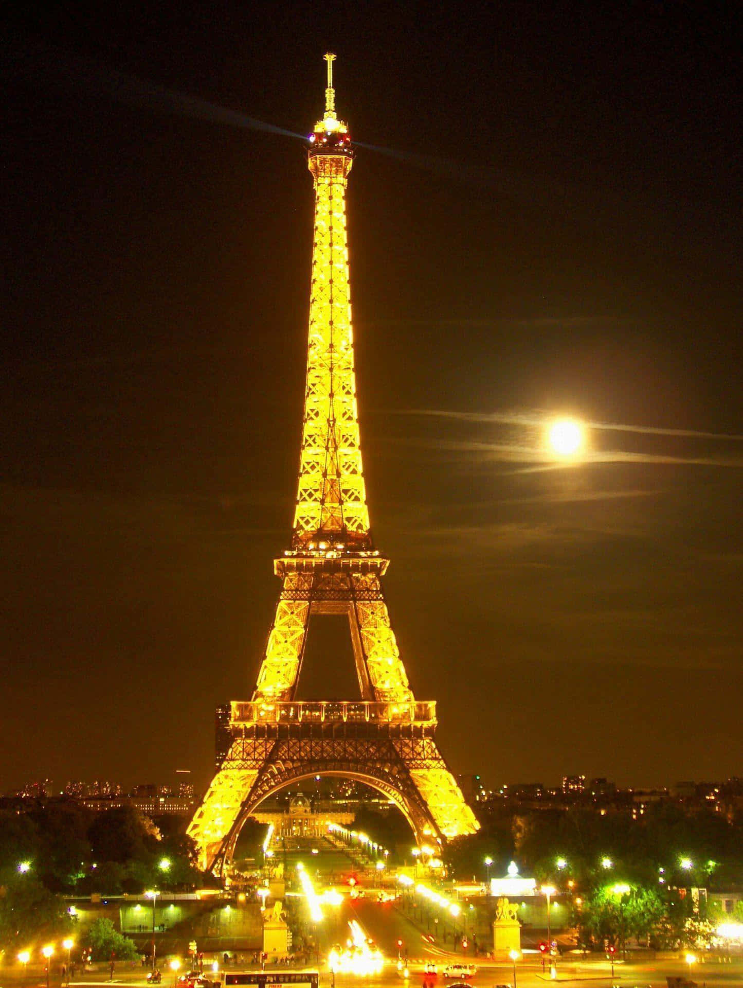 Eiffel Tower 桌布 壁紙 — 艾菲爾鐵塔在明亮的月光夜空下溫暖地發光，城市燈光在下方閃爍。
