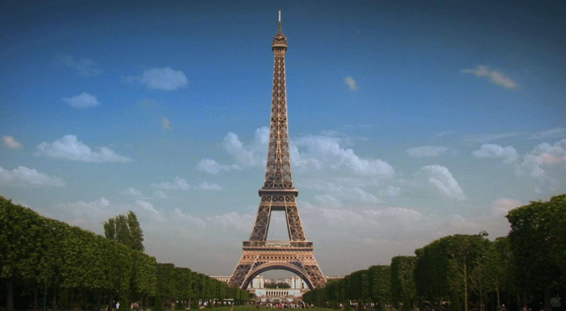 Paris Eiffel Tower 桌布 壁紙 — 艾菲爾鐵塔在明亮的藍天和白雲襯托下高聳入雲，兩旁對稱排列著茂密的綠樹。
