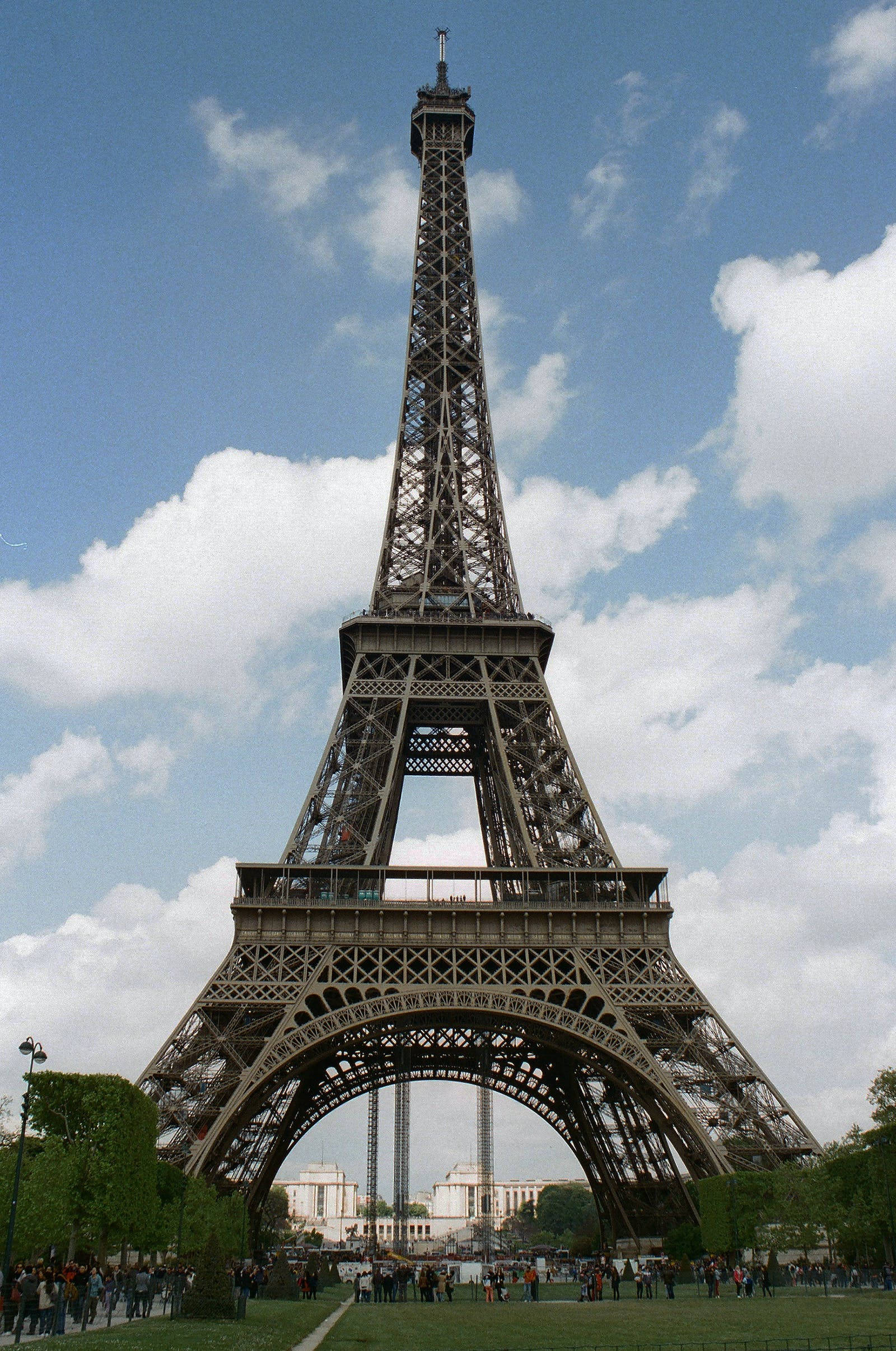 france iPhone 桌布 壁紙 — 艾菲爾鐵塔在明亮的藍天和白雲襯托下高聳入雲，遊客聚集在塔底。
