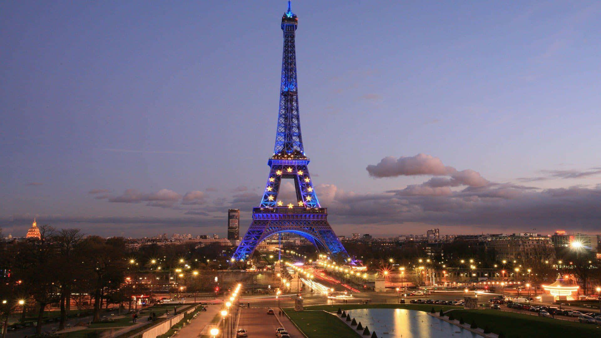 Eiffel Tower 桌布 壁紙 — 艾菲爾鐵塔在暮色天空下發出藍光，下方城市燈光在繁忙的巴黎場景中劃出線條。