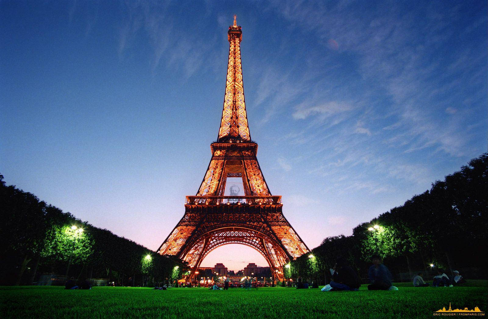 Paris Eiffel Tower 桌布 壁紙 — 艾菲爾鐵塔在暮色天空中溫暖地發光，人們在下面的草地上放鬆。