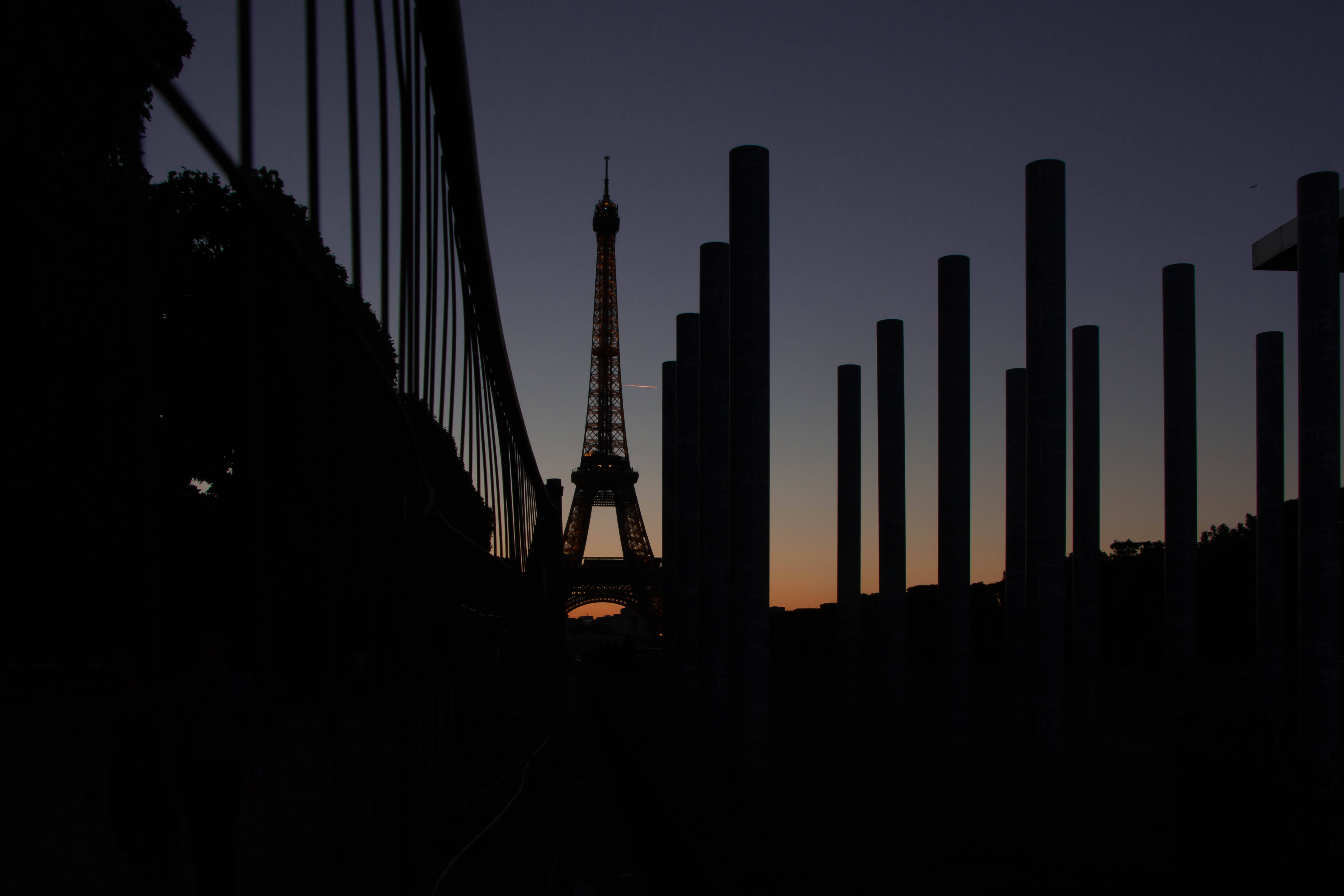 Eiffel Tower 桌布 壁紙 — 艾菲爾鐵塔在暮色天空中的剪影，被深色垂直柱子和欄杆框住。