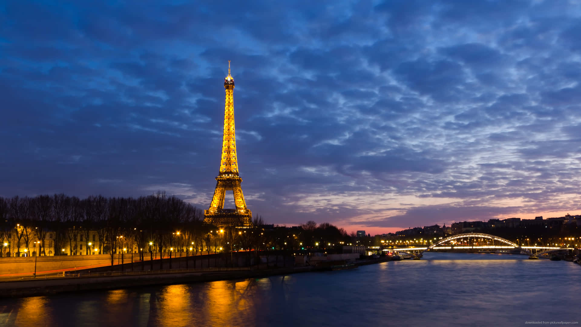 Eiffel Tower 桌布 壁紙 — 艾菲爾鐵塔在暮色天空中閃耀金色光芒，塞納河上倒映著柔和的粉紅和藍色雲彩。