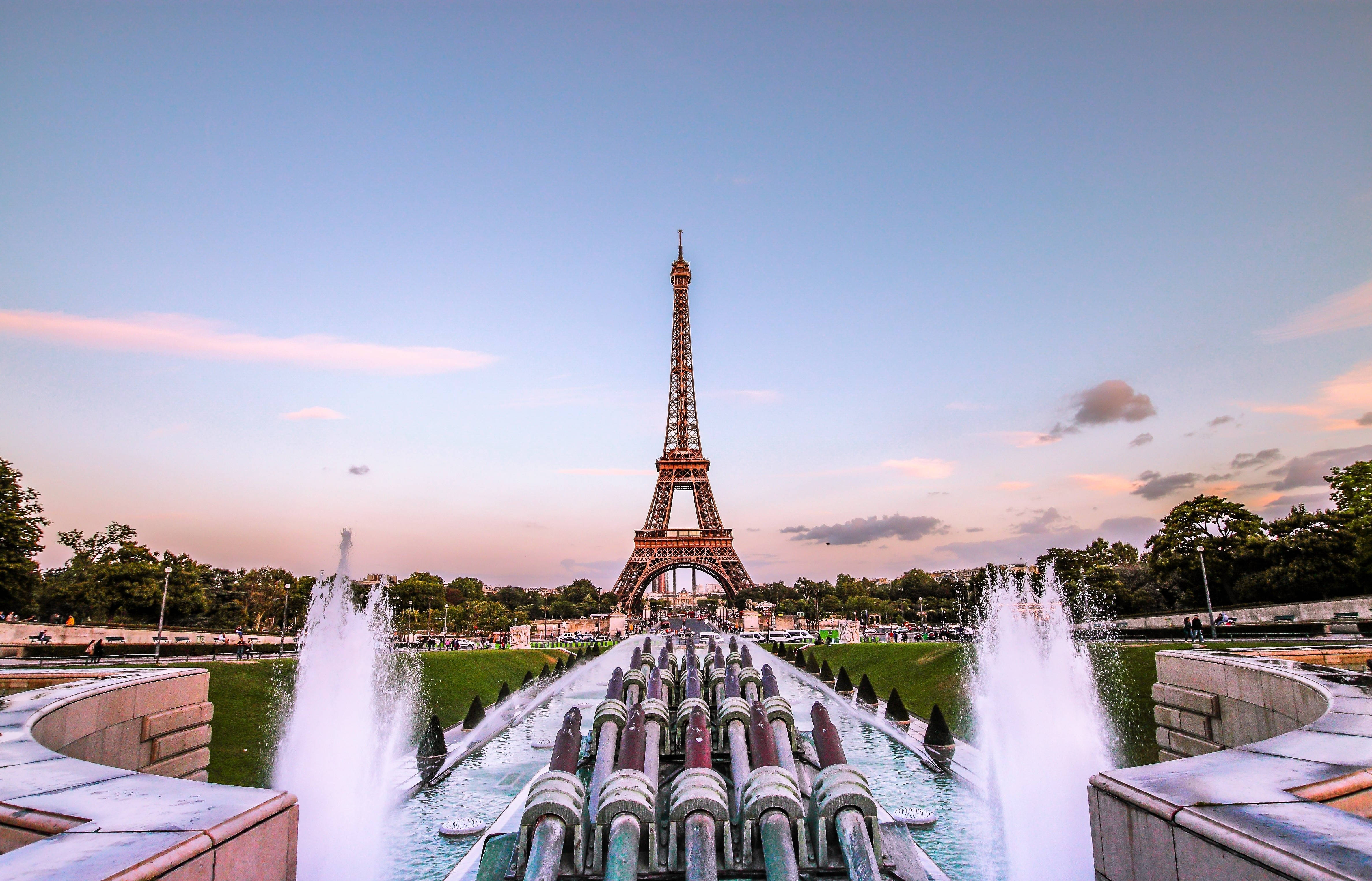 France 桌布 壁紙 — 艾菲爾鐵塔在柔和的暮色天空下巍然聳立，巴黎公園前景中的噴泉噴灑著水花。