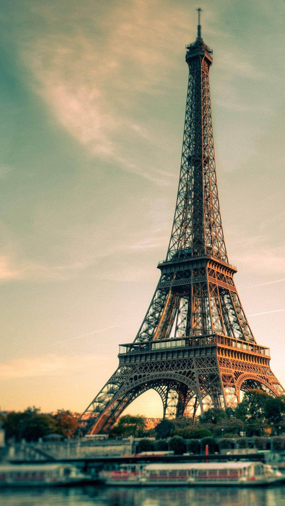 Paris Eiffel Tower 桌布 壁紙 — 艾菲爾鐵塔在柔和的金色日落天空下高聳，一艘河船在其標誌性的鐵格架下滑行。