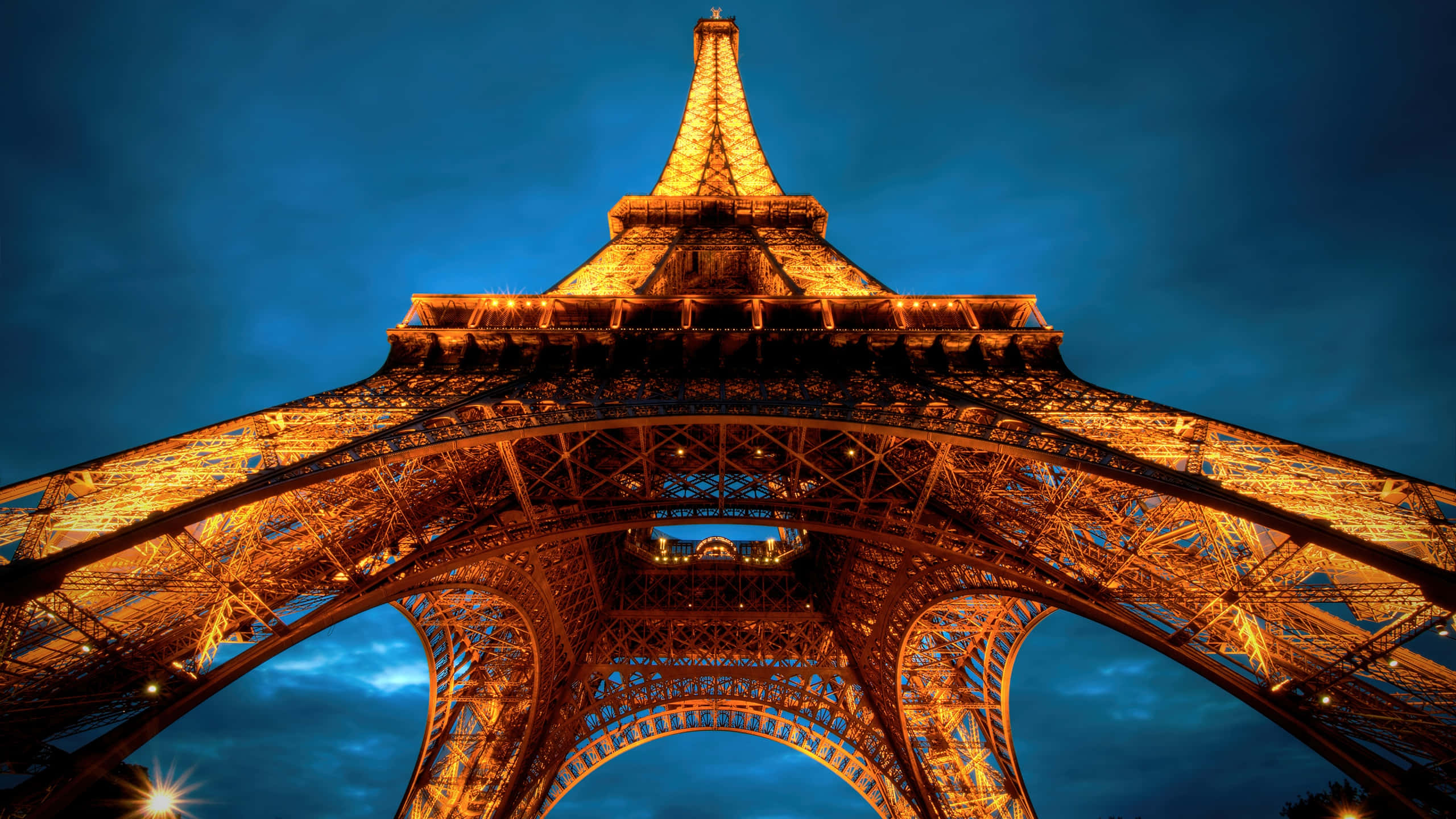Paris At Night 桌布 壁紙 — 艾菲爾鐵塔在深藍色暮色天空下以金色燈光點亮，從戲劇性的低角度拍攝。
