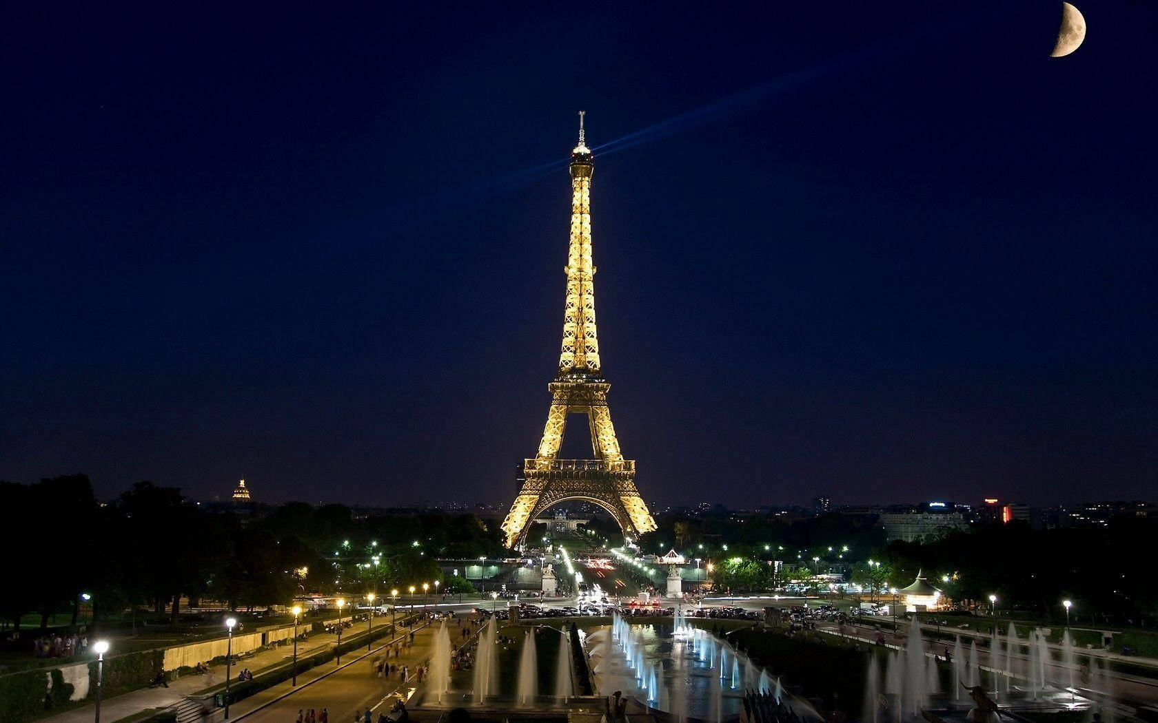Paris Eiffel Tower 桌布 壁紙 — 艾菲爾鐵塔在深藍色的夜空中閃耀著金色光芒，新月和城市燈光倒映在下面的噴泉中。