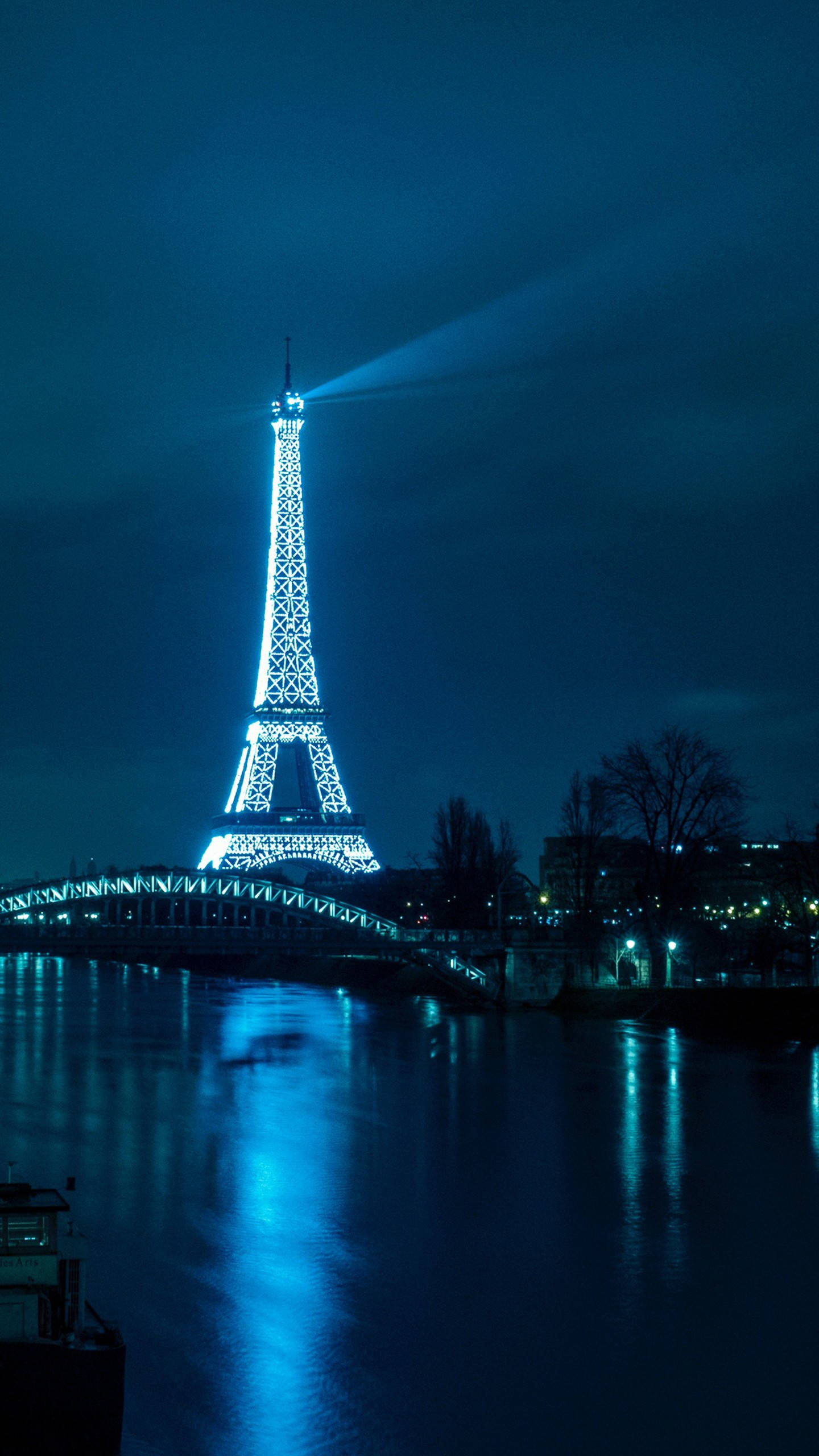 Eiffel Tower 桌布 壁紙 — 艾菲爾鐵塔在深藍色的夜空中閃耀著明亮的白光，其光束劃過塞納河上方的空氣。