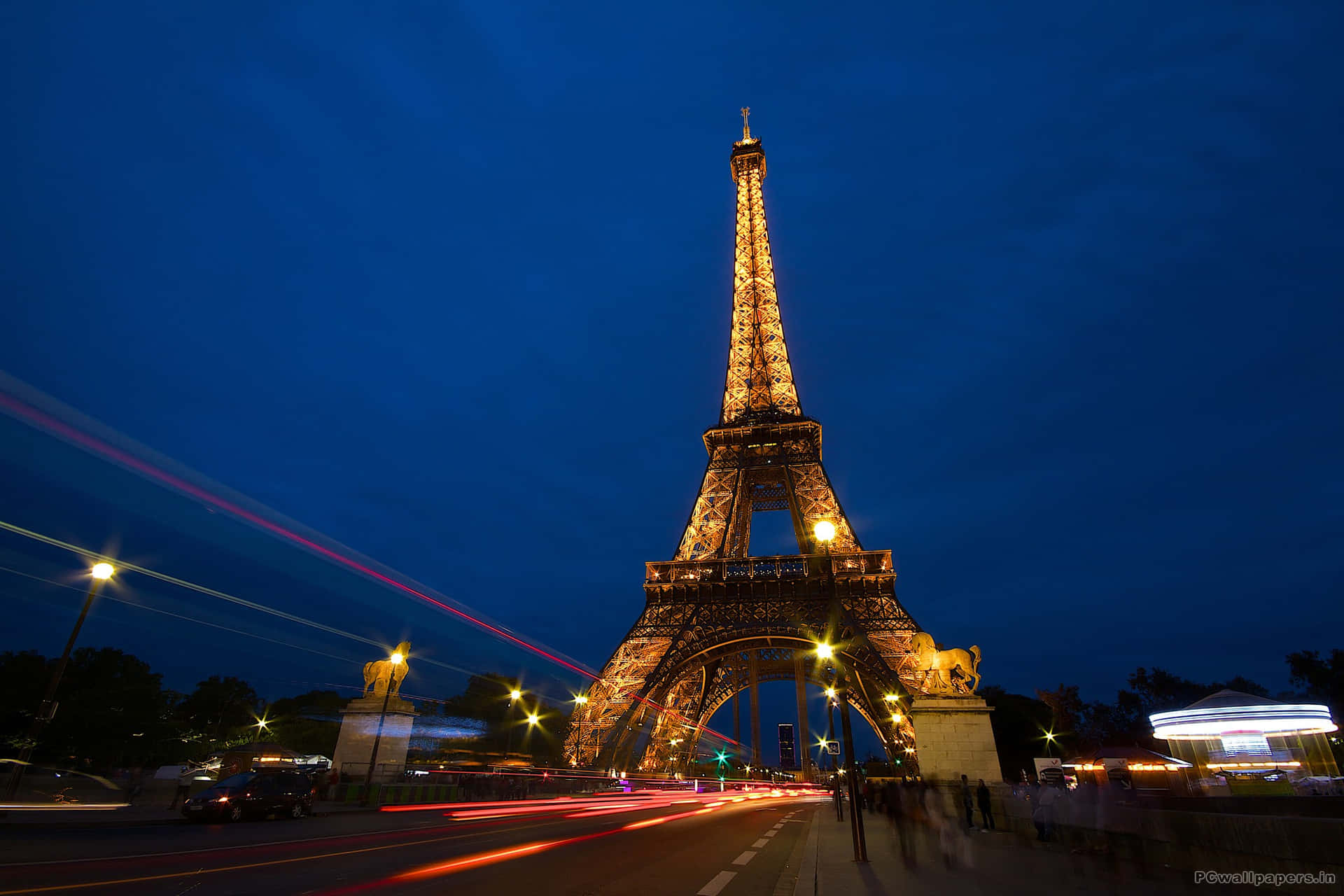 Eiffel Tower 桌布 壁紙 — 艾菲爾鐵塔在深藍色的暮色中溫暖地發光，前景中汽車燈光的條紋模糊地掠過。