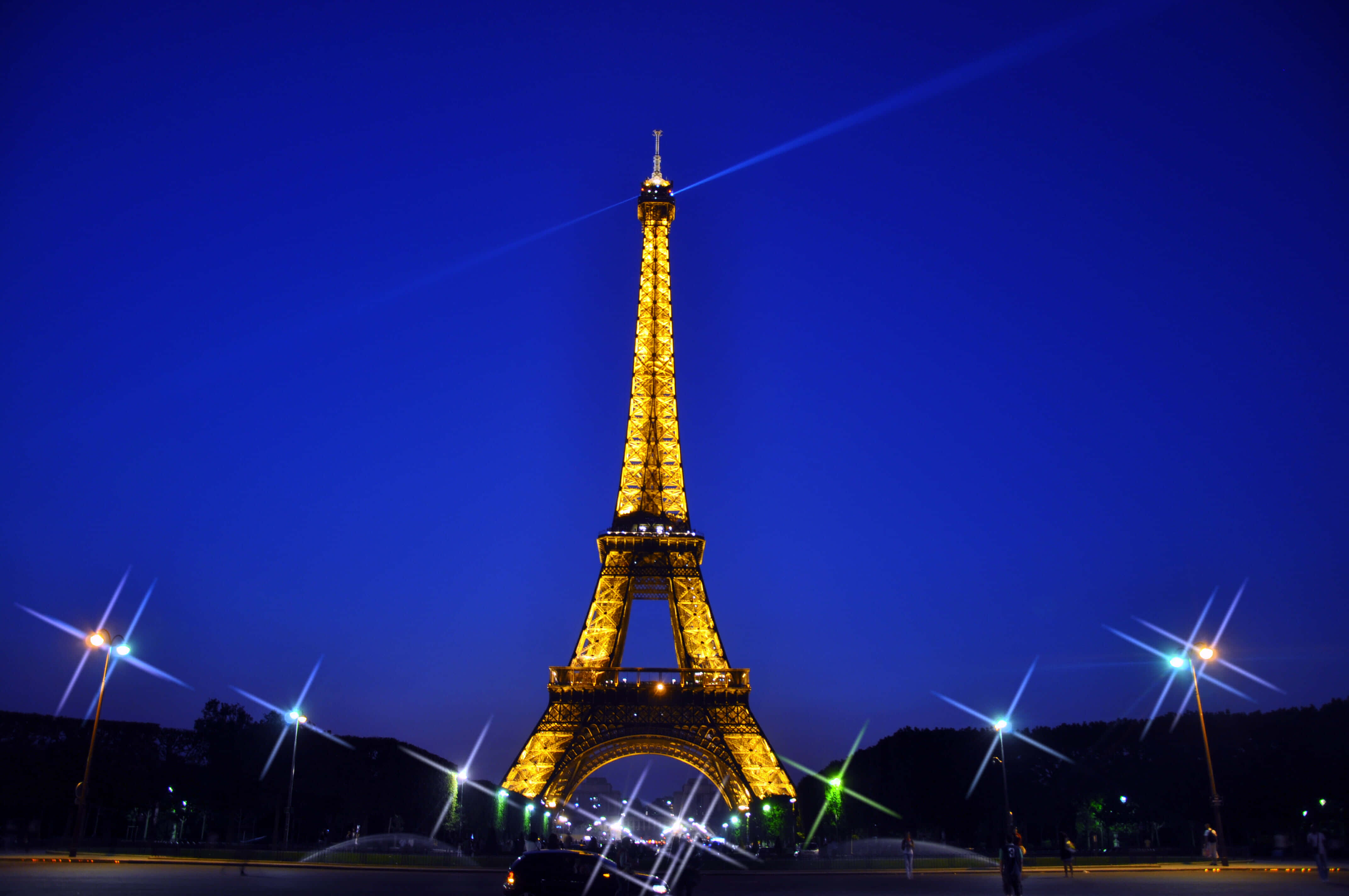Eiffel Tower 桌布 壁紙 — 艾菲爾鐵塔在深藍色的暮色天空中閃耀著金色光芒，星芒狀的路燈襯托著這個標誌性的巴黎地標。