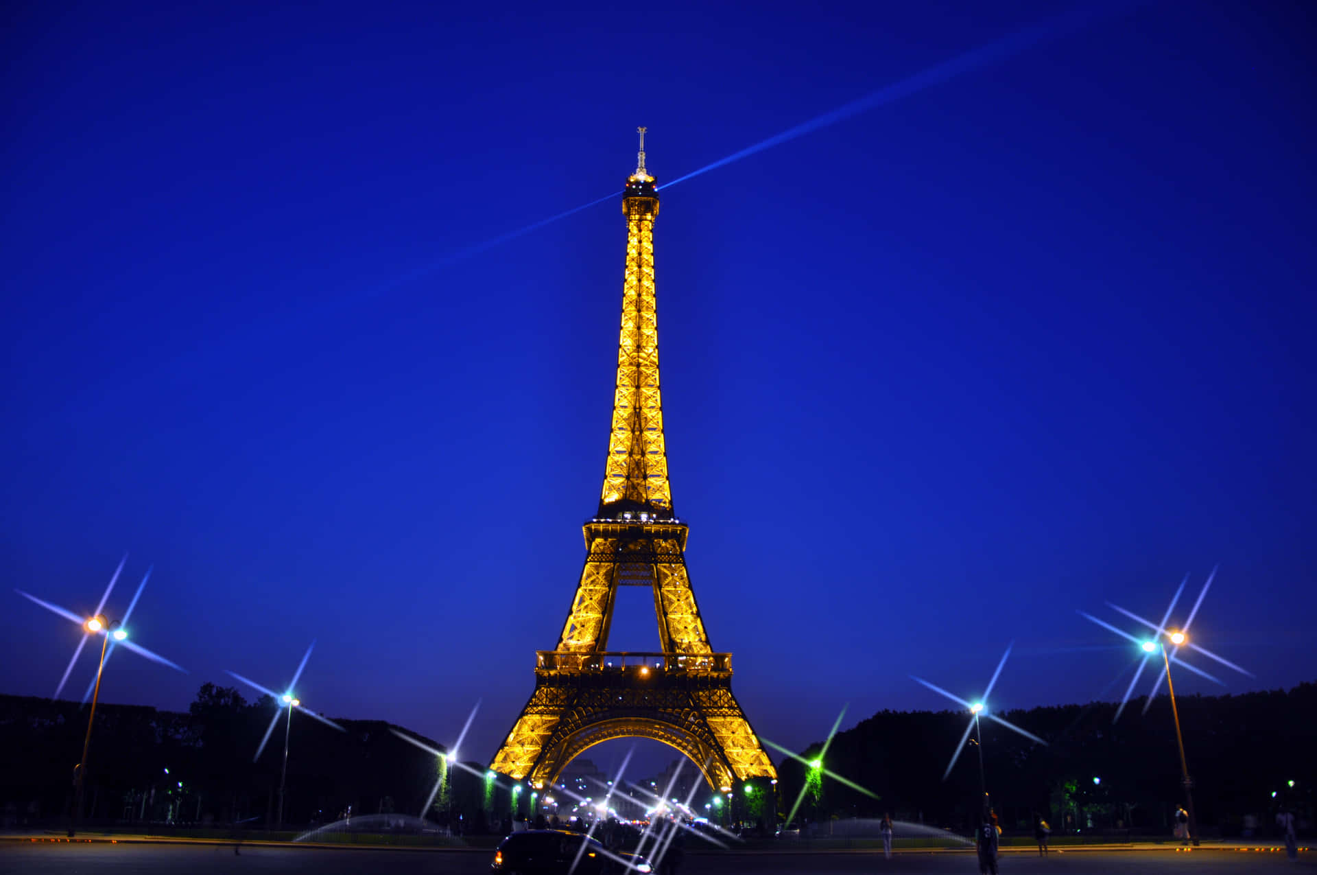 Eiffel Tower 桌布 壁紙 — 艾菲爾鐵塔在深藍色的暮色天空中閃耀著金色光芒，星芒狀的路燈襯托著這個標誌性的巴黎地標。