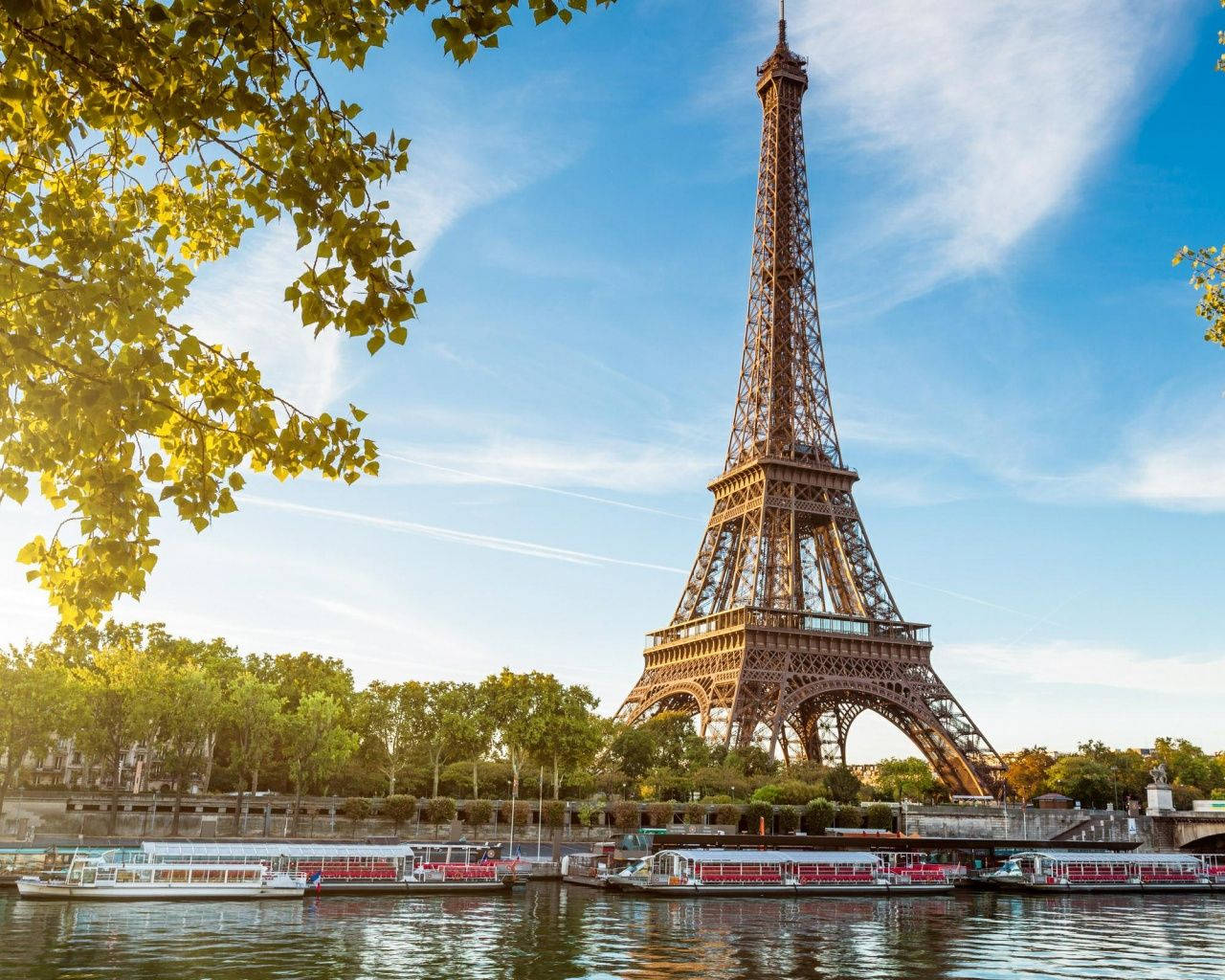 Eiffel Tower 桌布 壁紙 — 艾菲爾鐵塔在清澈的藍天下高聳，金色的樹葉框住場景，船隻在下面的塞納河上漂浮。
