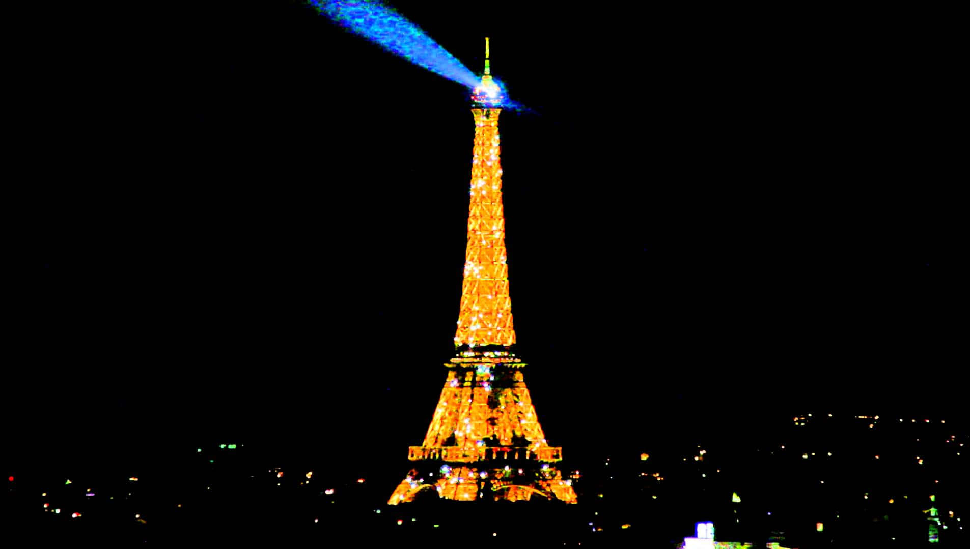 Eiffel Tower 桌布 壁紙 — 艾菲爾鐵塔在漆黑的夜空下溫暖地發光，一道鮮豔的藍色雷射光束從其頂部向上射出。