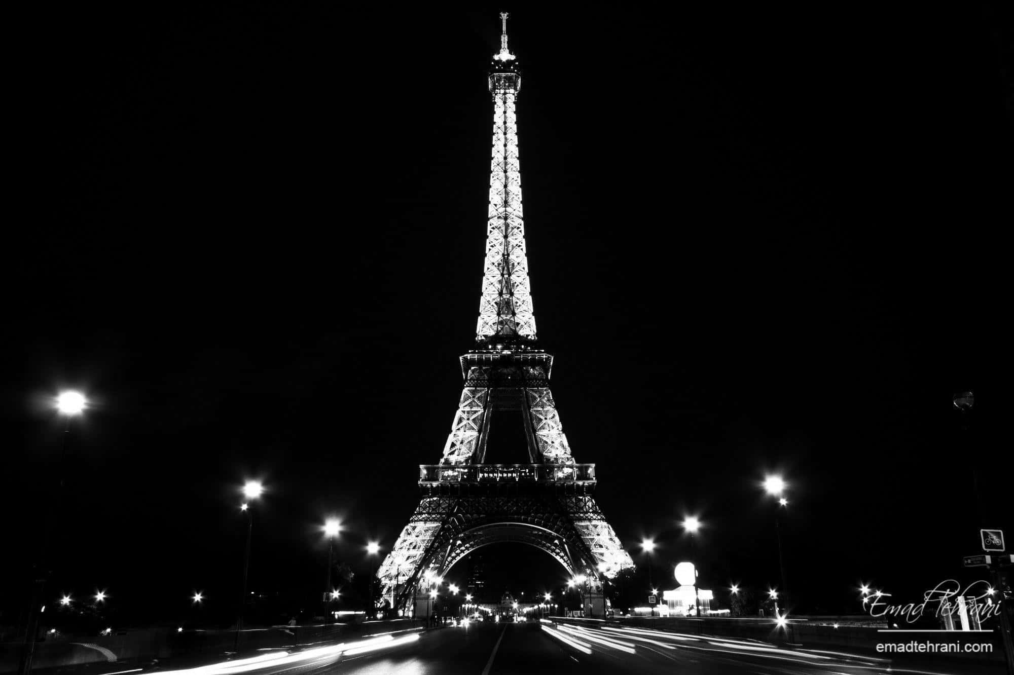 Eiffel Tower 桌布 壁紙 — 艾菲爾鐵塔在漆黑的夜空中亮起，下方有汽車駛過留下的光軌。
