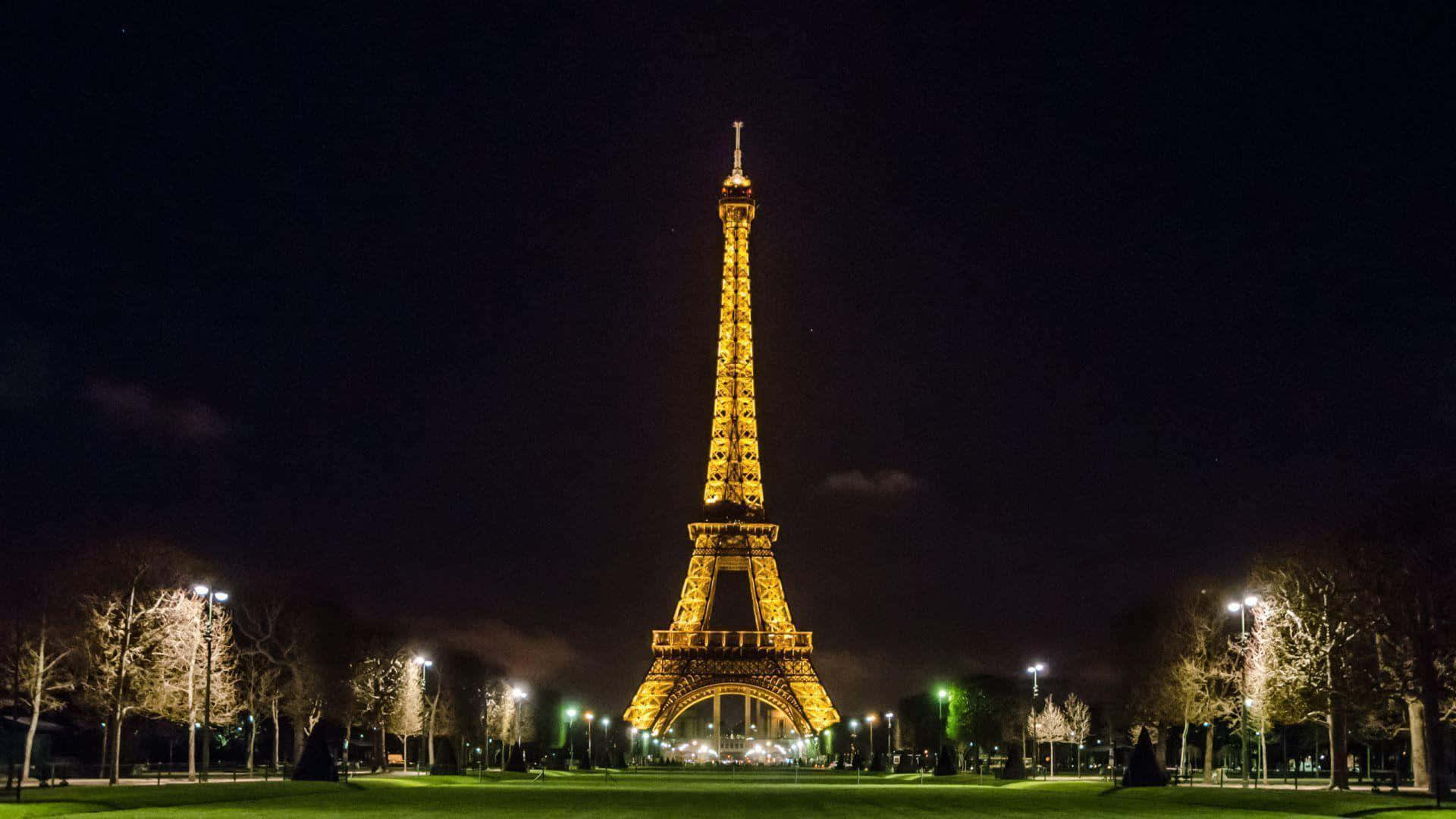 Eiffel Tower 桌布 壁紙 — 艾菲爾鐵塔在漆黑的夜空中散發溫暖的光芒，周圍是燈火通明的樹木和寧靜的公園。