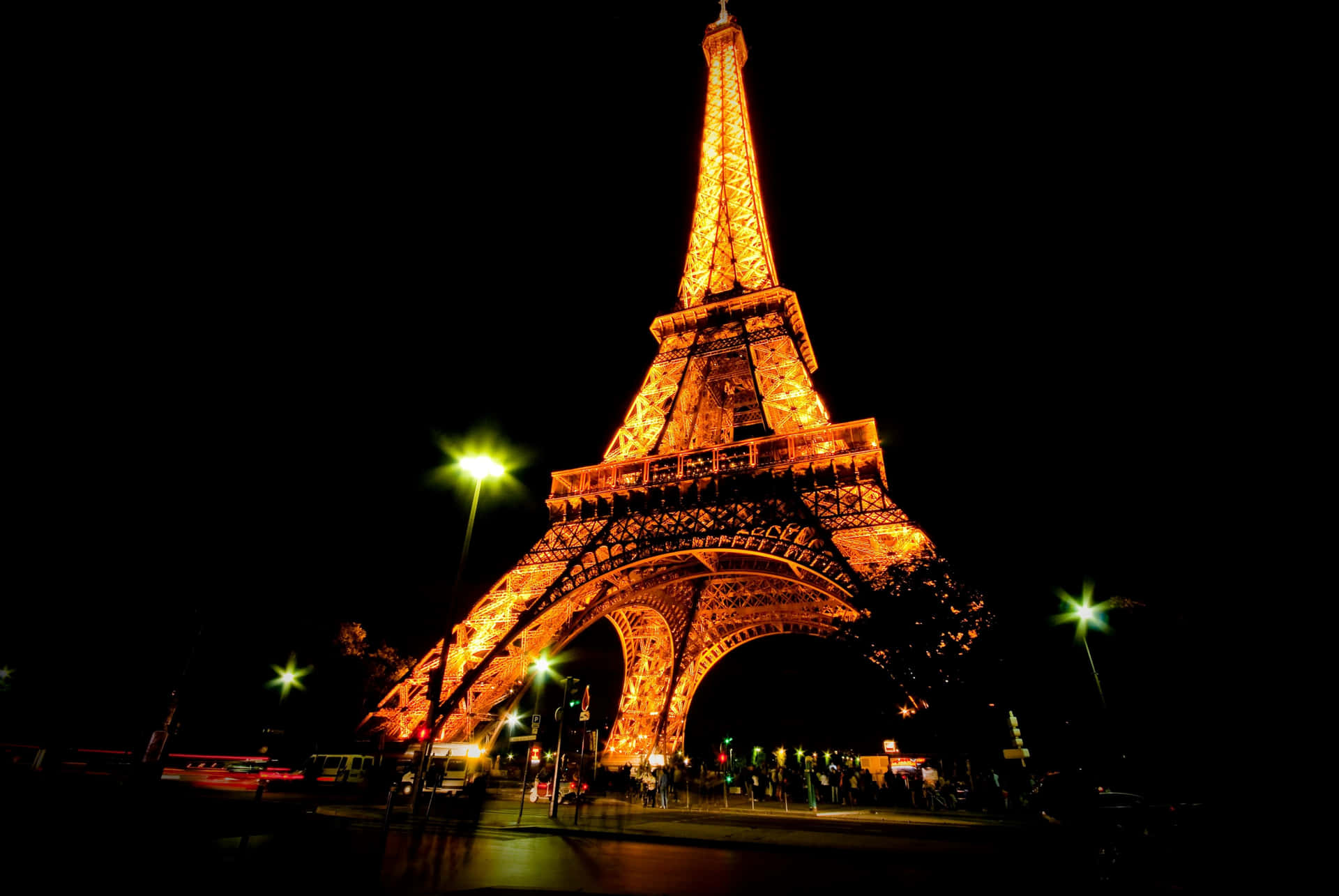 Eiffel Tower 桌布 壁紙 — 艾菲爾鐵塔在漆黑的夜空中溫暖地發光，明亮的綠色街燈照亮了下方潮濕的路面。