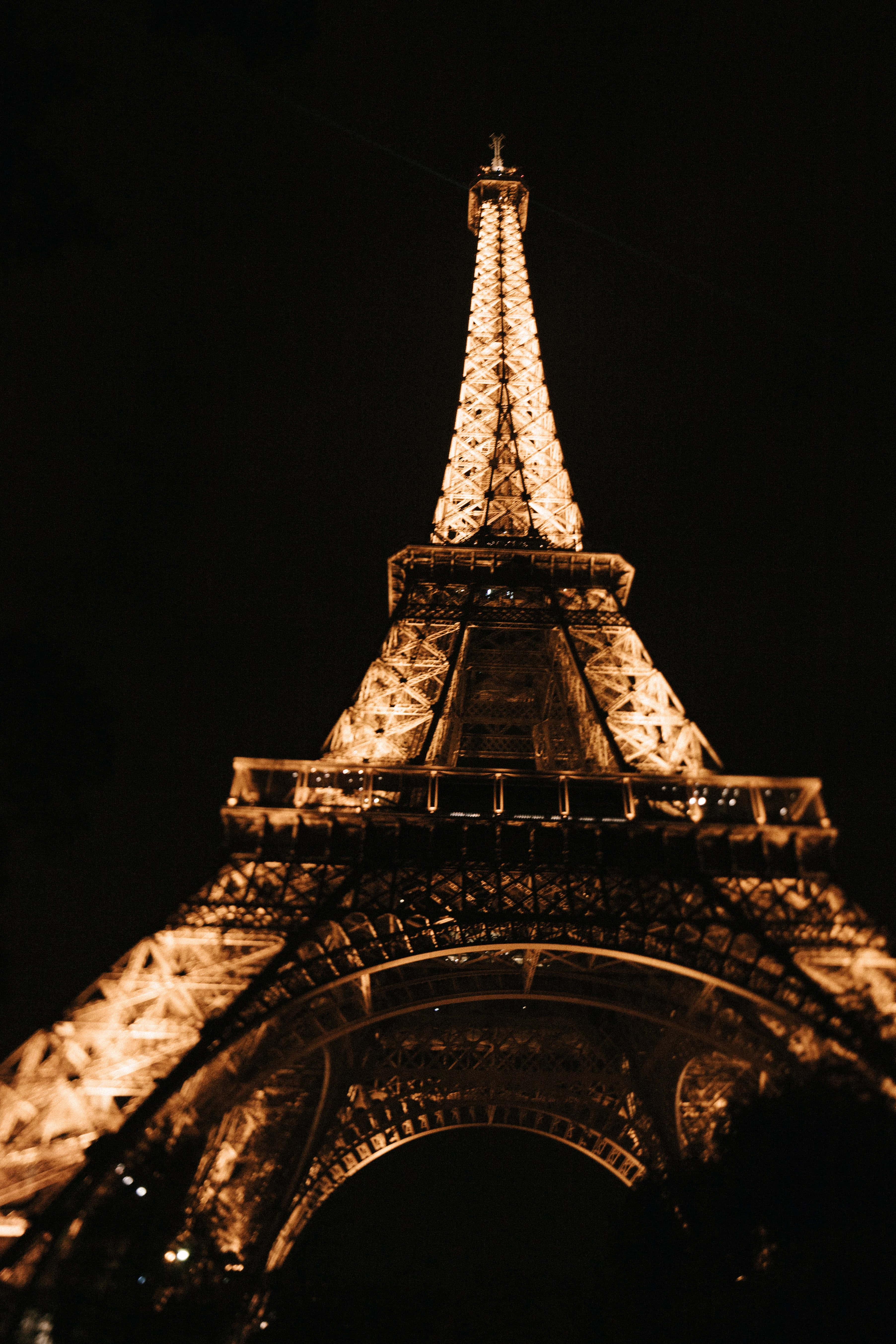 Paris At Night 桌布 壁紙 — 艾菲爾鐵塔在漆黑的夜空中溫暖地發光，以戲劇性的低角度拍攝。
