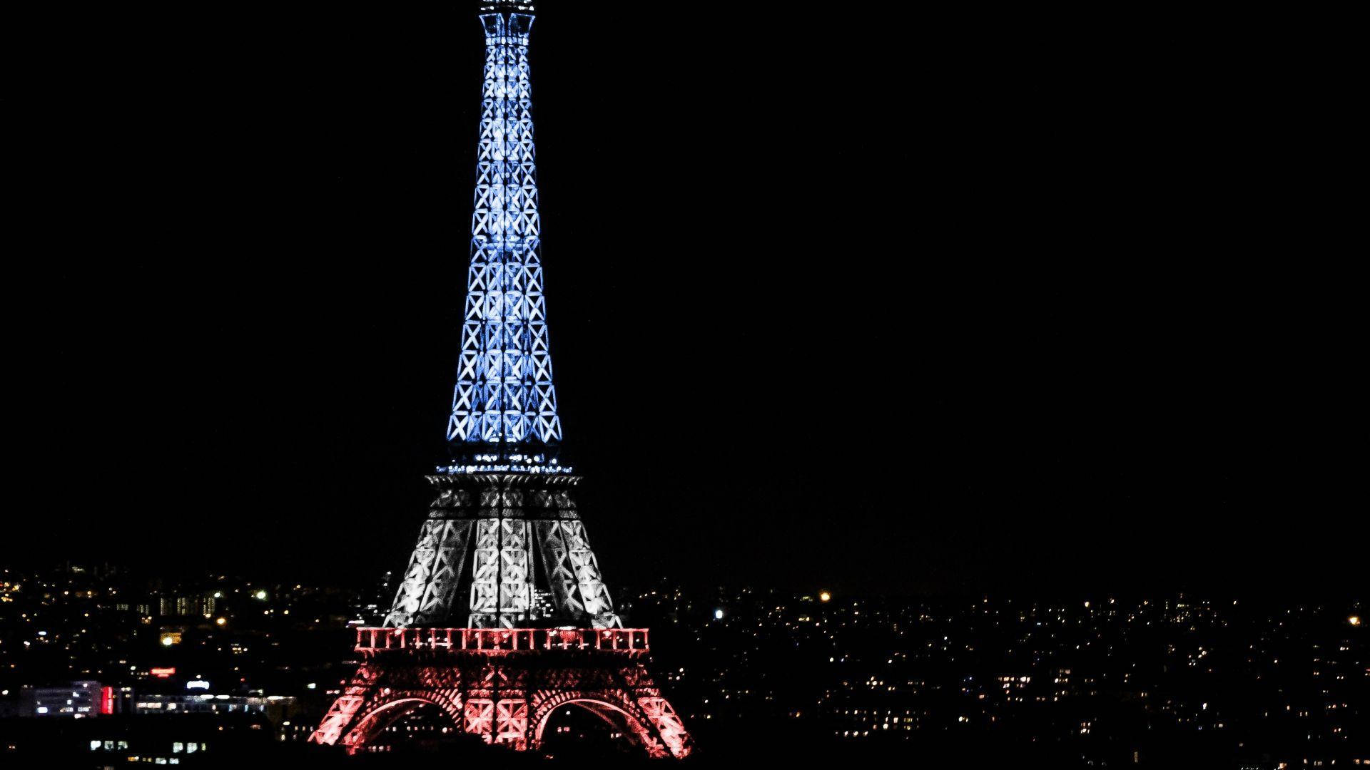 Eiffel Tower 桌布 壁紙 — 艾菲爾鐵塔在漆黑的夜空中閃爍著藍色和紅色的燈光，下方城市燈光閃爍。