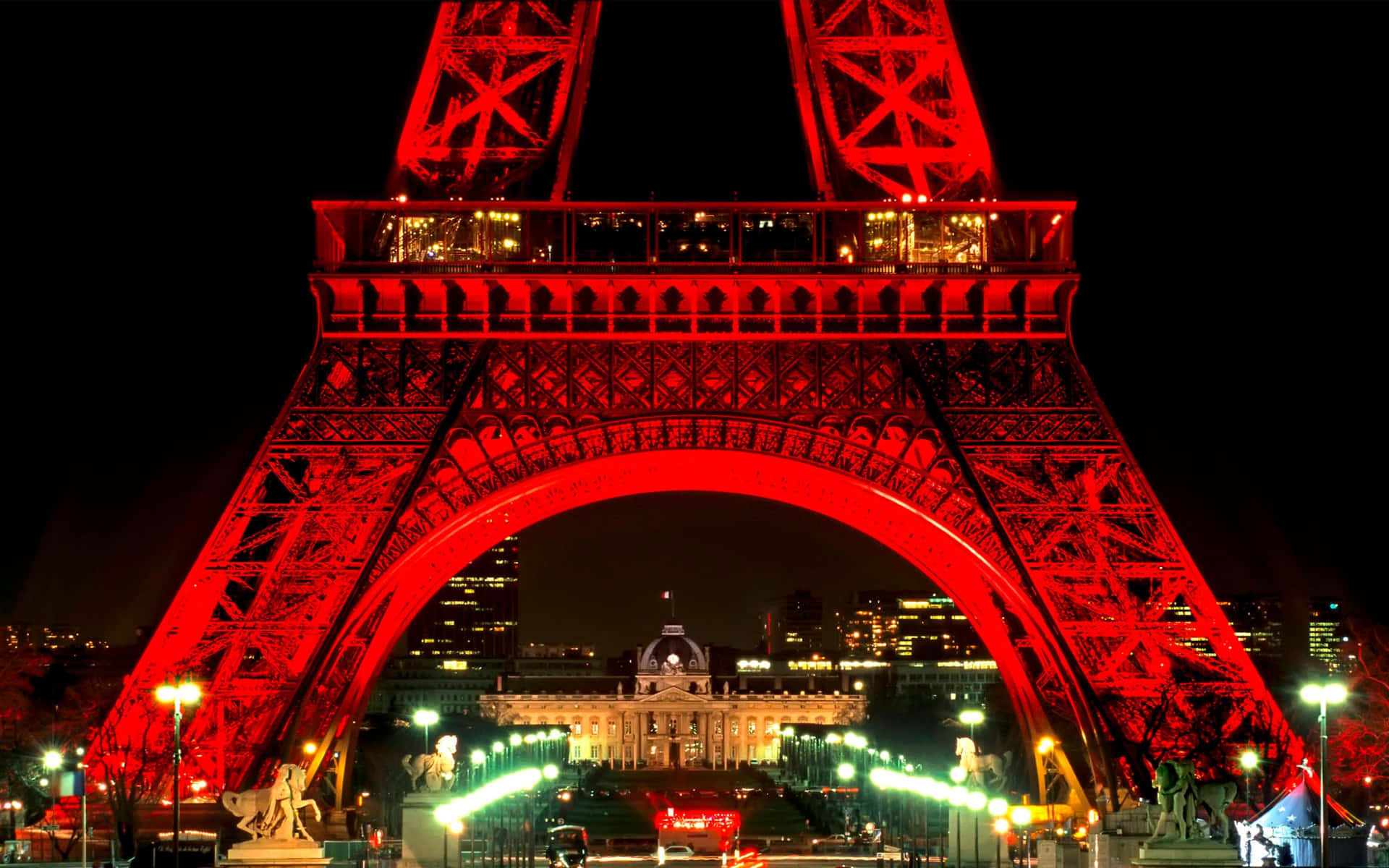 Paris At Night 桌布 壁紙 — 艾菲爾鐵塔在漆黑的夜空中閃耀著鮮豔的紅色，透過拱門可以看到燈火通明的城市景觀。