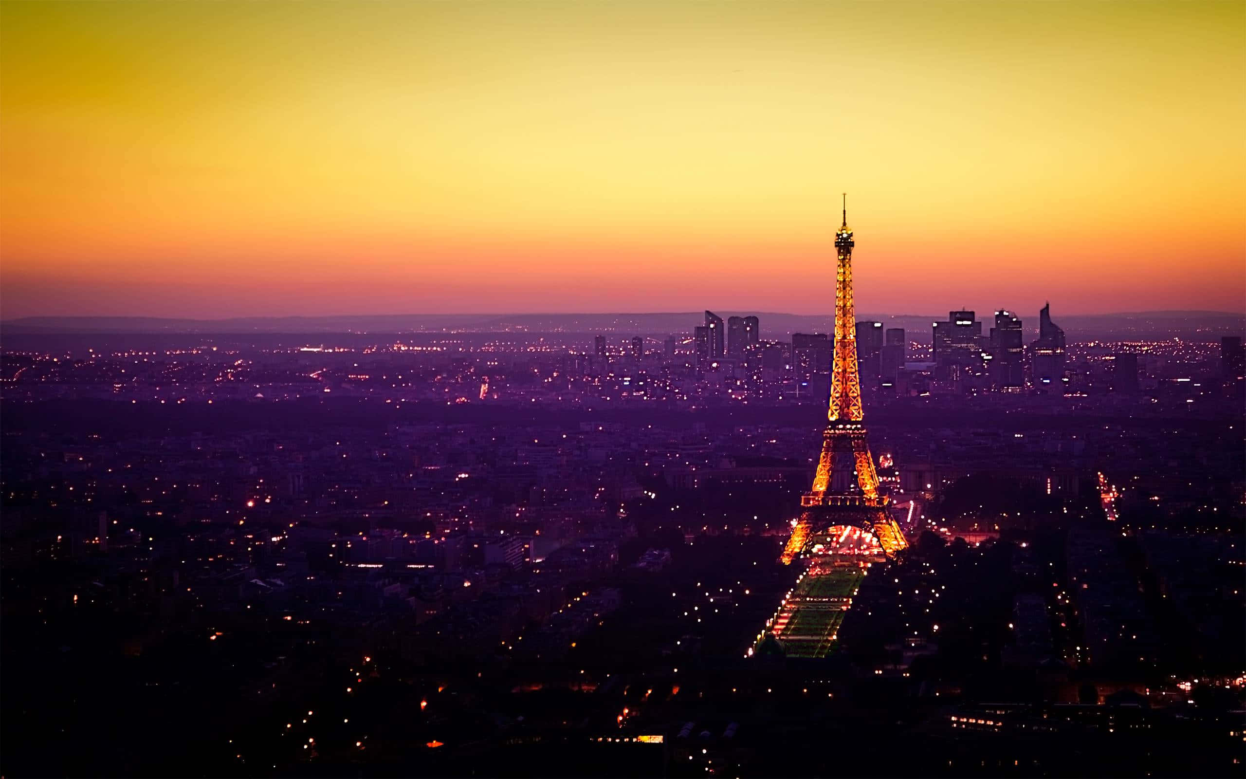 Eiffel Tower 桌布 壁紙 — 艾菲爾鐵塔在火紅的夕陽天空下閃耀金光，巴黎的城市燈光在下方閃爍。