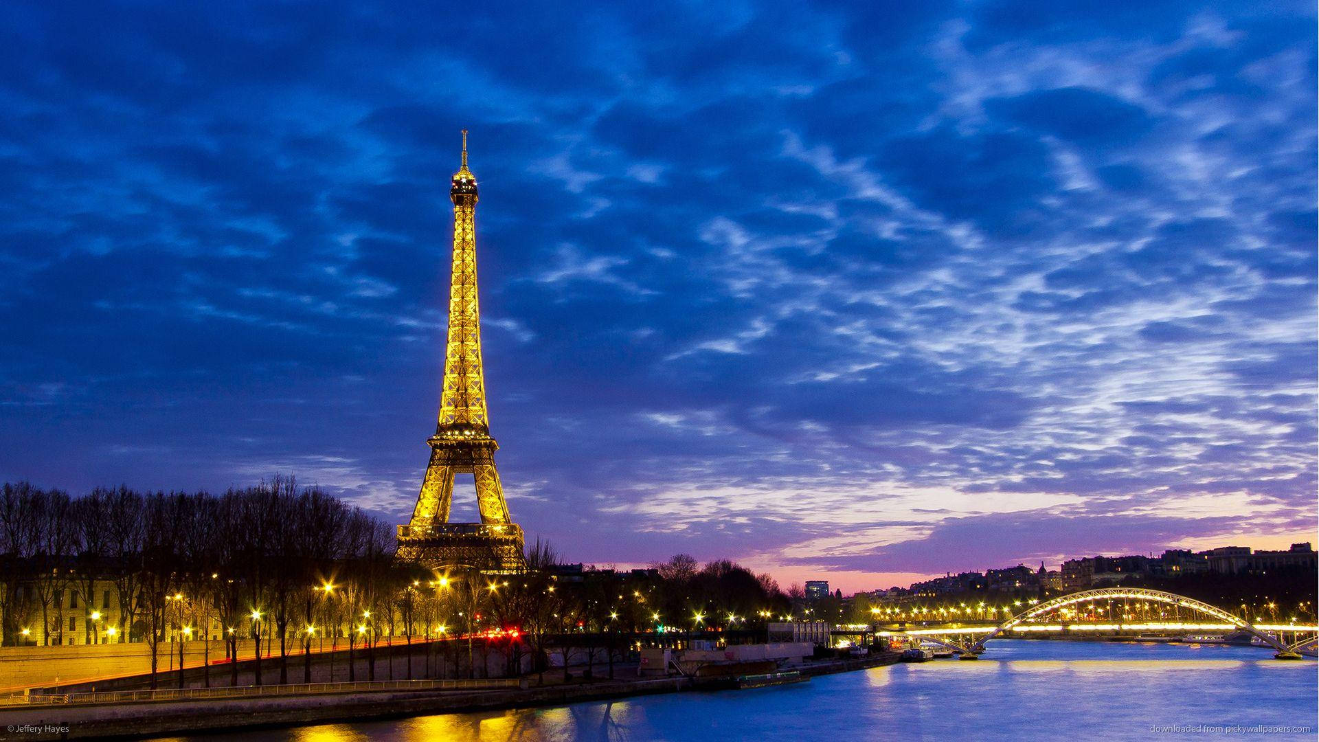 Paris Eiffel Tower 桌布 壁紙 — 艾菲爾鐵塔在紫色和藍色雲彩倒映在塞納河的戲劇性暮色天空下閃耀著金色光芒。