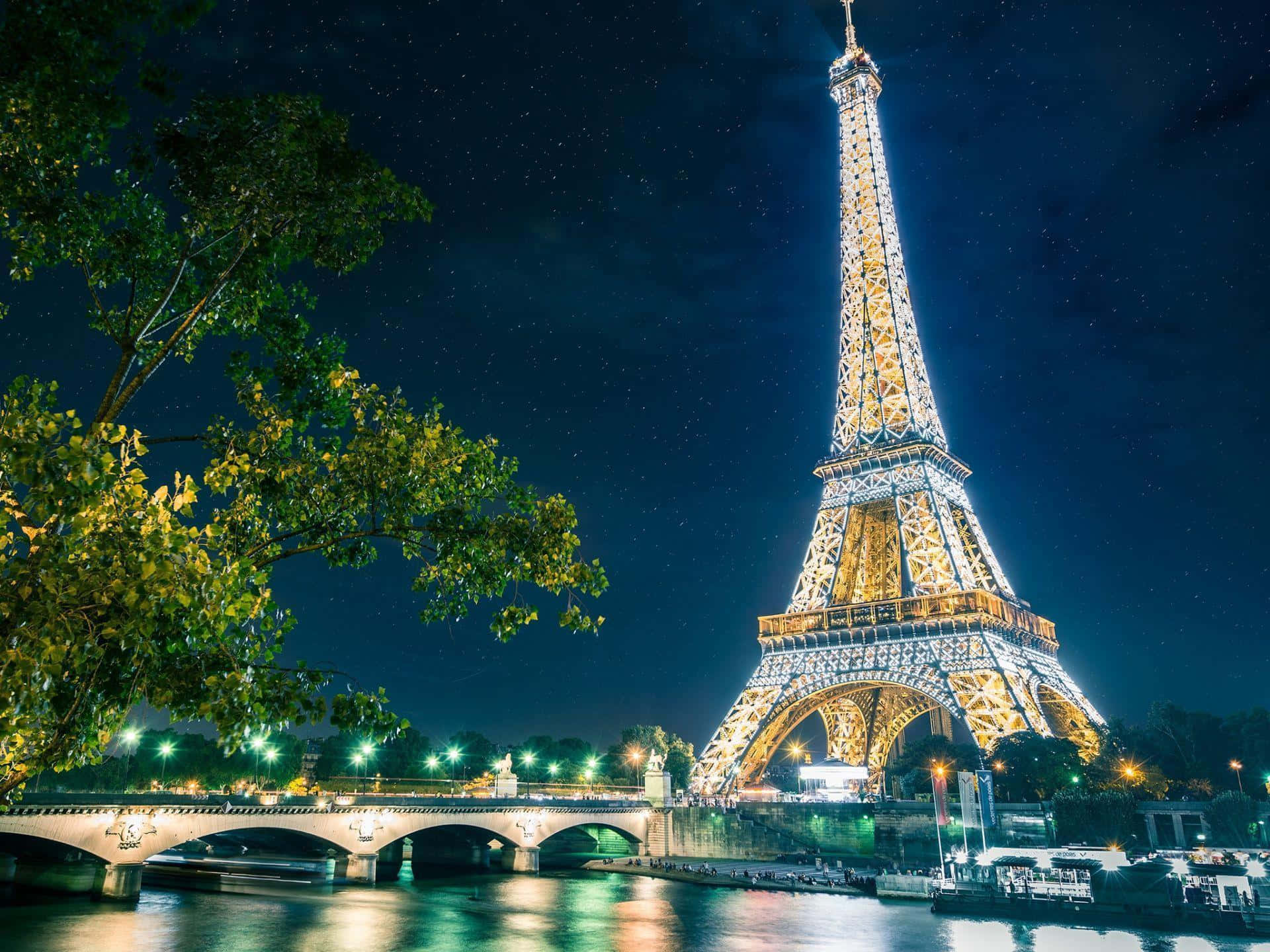 Eiffel Tower 桌布 壁紙 — 艾菲爾鐵塔在繁星點點的夜空下閃耀，倒映在塞納河中，橋樑和樹木環繞著這個標誌性的巴黎地標。