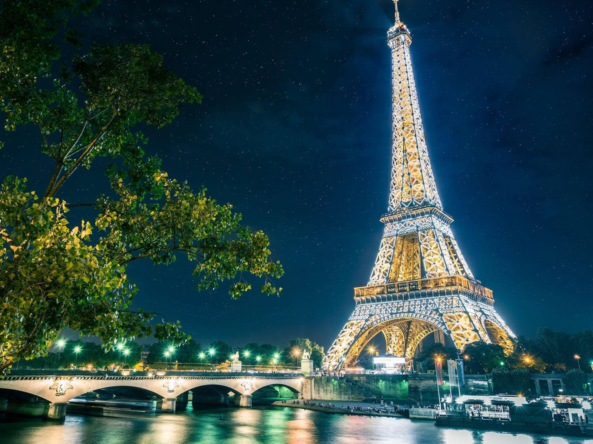 Eiffel Tower 桌布 壁紙 — 艾菲爾鐵塔在繁星點點的夜空下閃耀，倒映在塞納河中，橋樑和樹木襯托著這個標誌性的巴黎地標。