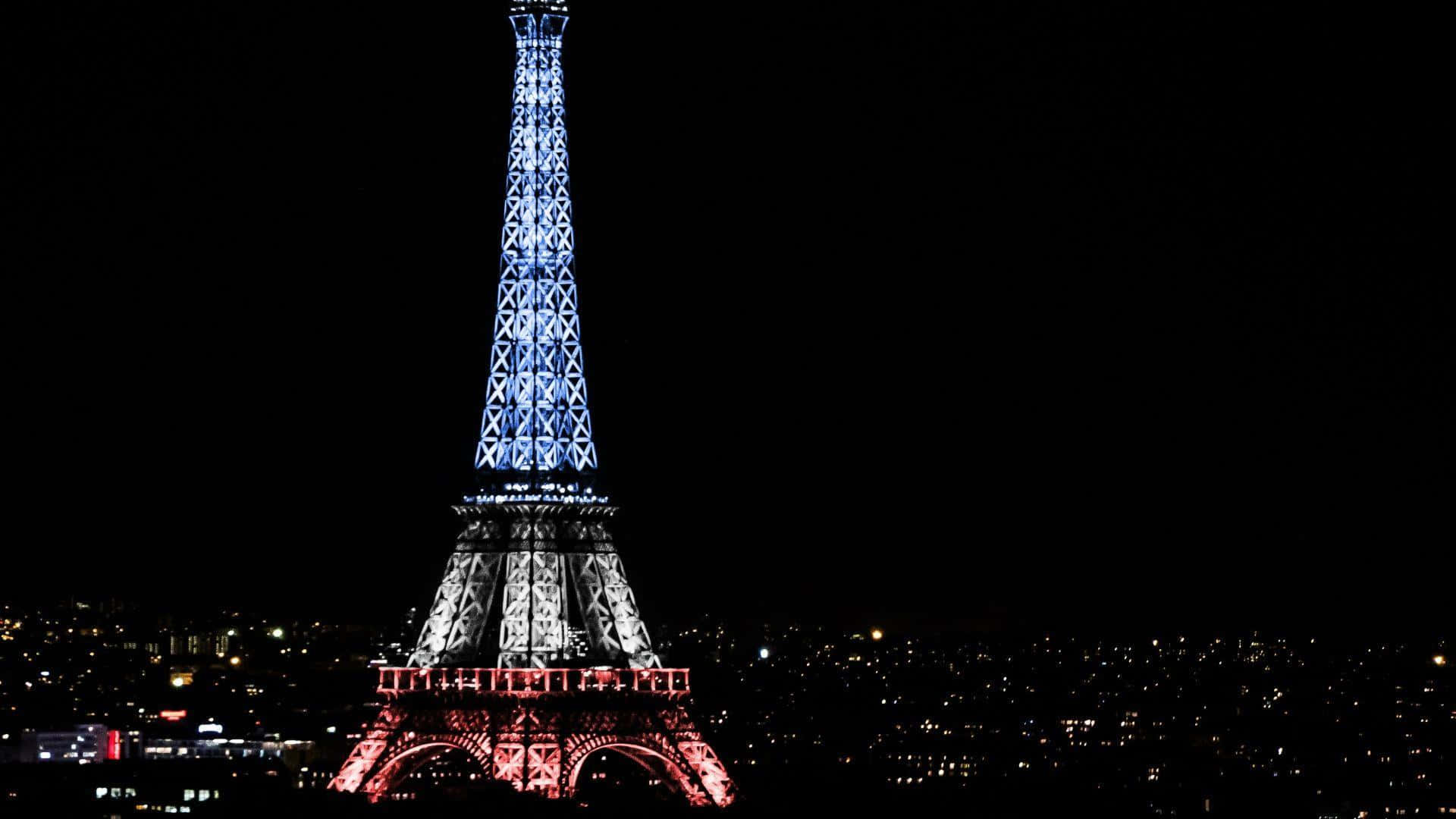 Eiffel Tower 桌布 壁紙 — 艾菲爾鐵塔在藍色和紅色燈光下照亮，背景是黑暗的夜空和下方的城市燈光。
