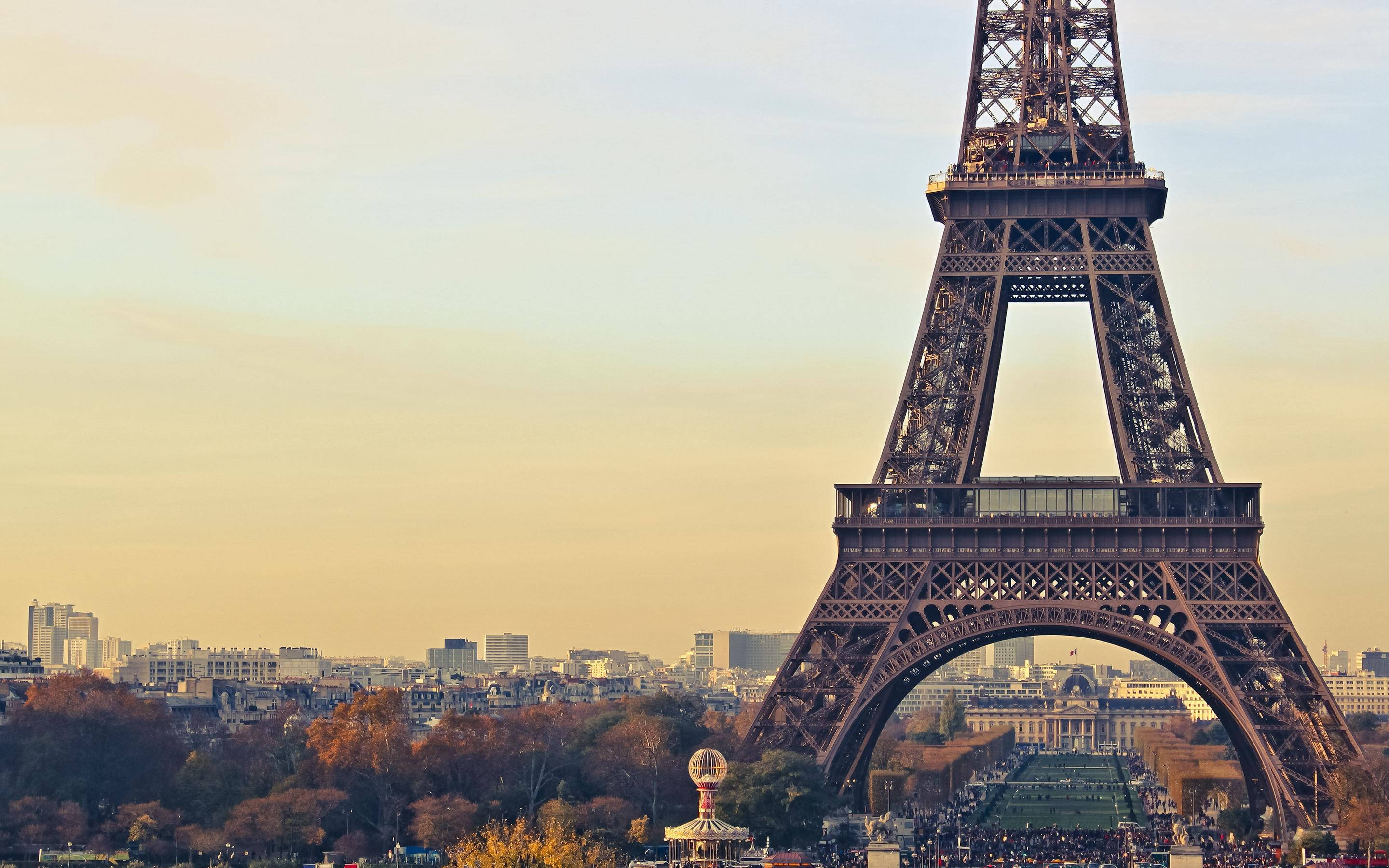 Paris Eiffel Tower 桌布 壁紙 — 艾菲爾鐵塔在金色夕陽天空下高聳，背景有秋天的樹木和巴黎屋頂。