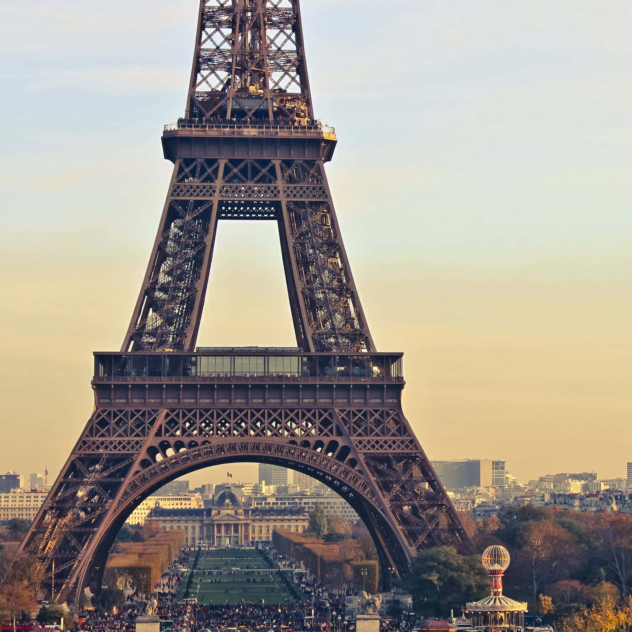 Eiffel Tower 桌布 壁紙 — 艾菲爾鐵塔在金色夕陽天空下高聳矗立，下方是巴黎的屋頂和熱鬧的戰神廣場。
