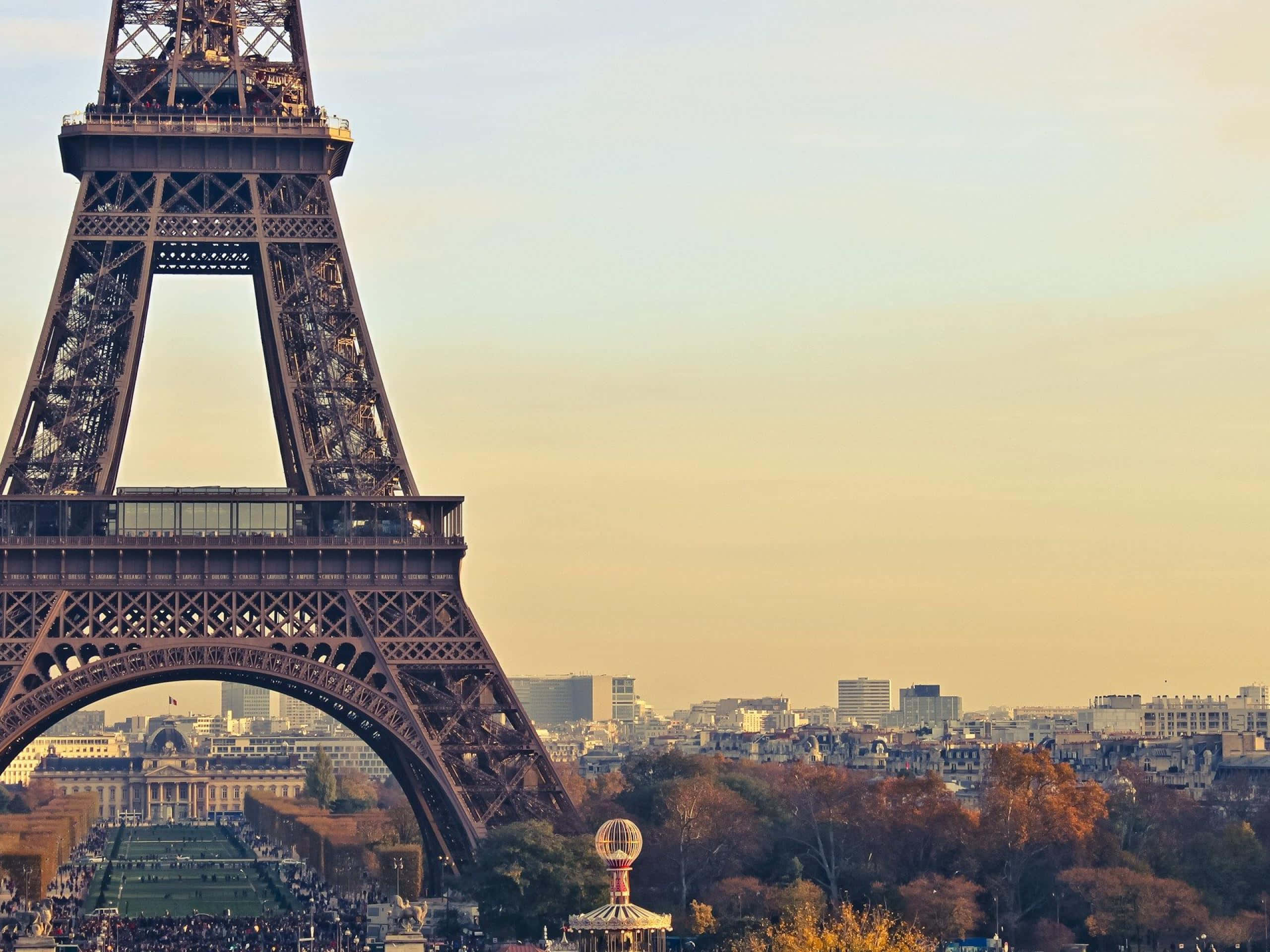 Paris Desktop 桌布 壁紙 — 艾菲爾鐵塔在金色日落天空下高聳矗立，下方是秋日樹木和巴黎屋頂。