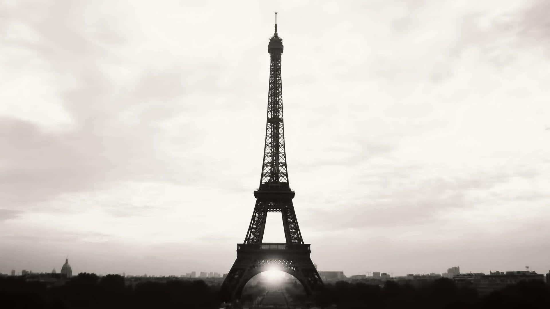 Eiffel Tower 桌布 壁紙 — 艾菲爾鐵塔在陰雲密佈的天空下，以清晰的剪影矗立，陽光穿過其拱門閃耀。