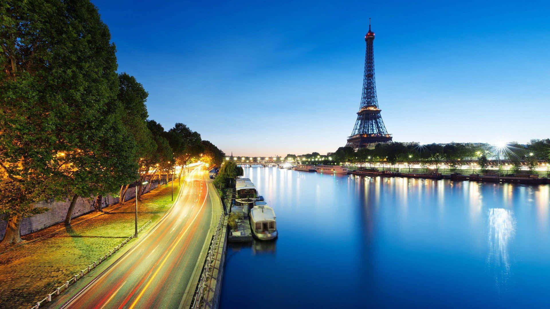 Eiffel Tower 桌布 壁紙 — 艾菲爾鐵塔在黃昏時分於塞納河上閃耀，交通和停泊船隻的光跡在平靜的水面上反射。