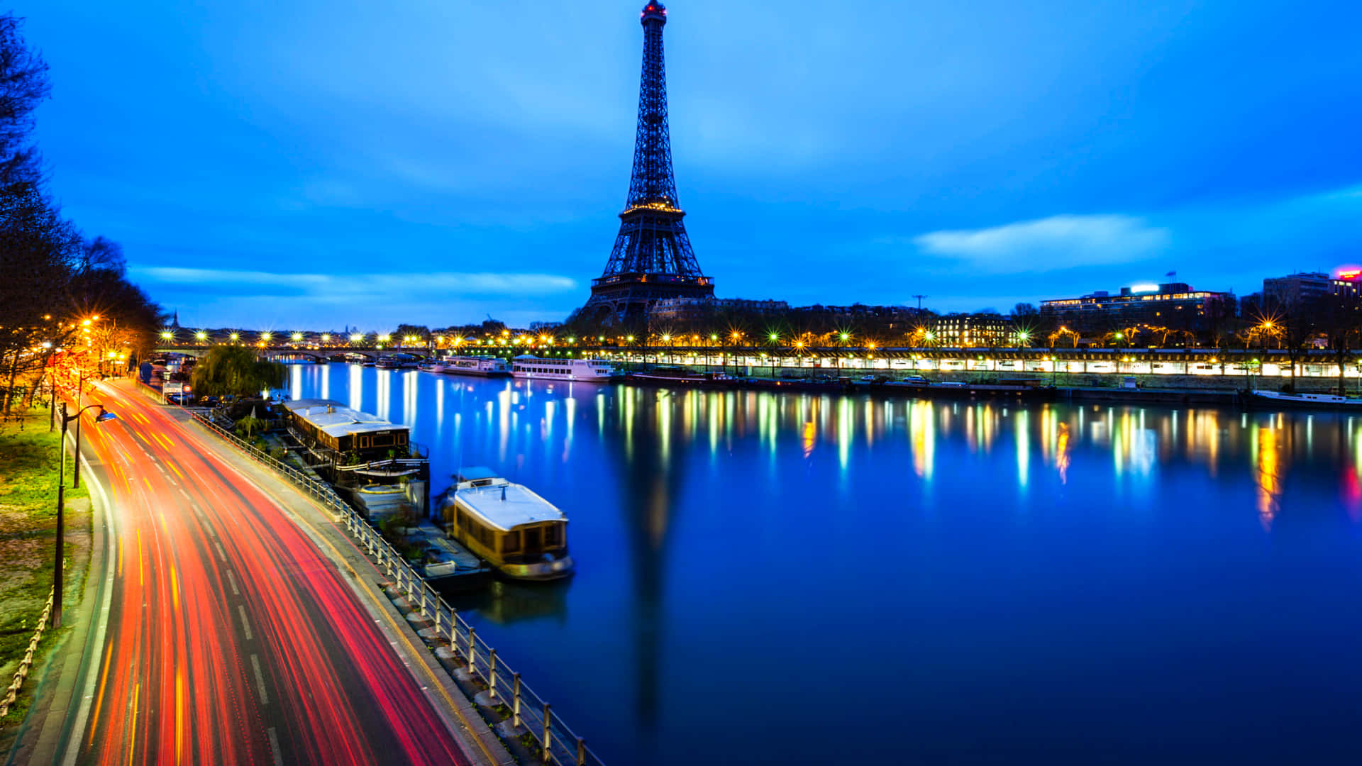 Paris Desktop 桌布 壁紙 — 艾菲爾鐵塔在黃昏時分發光，倒映在塞納河中，紅色車燈的條紋沿河岸模糊。