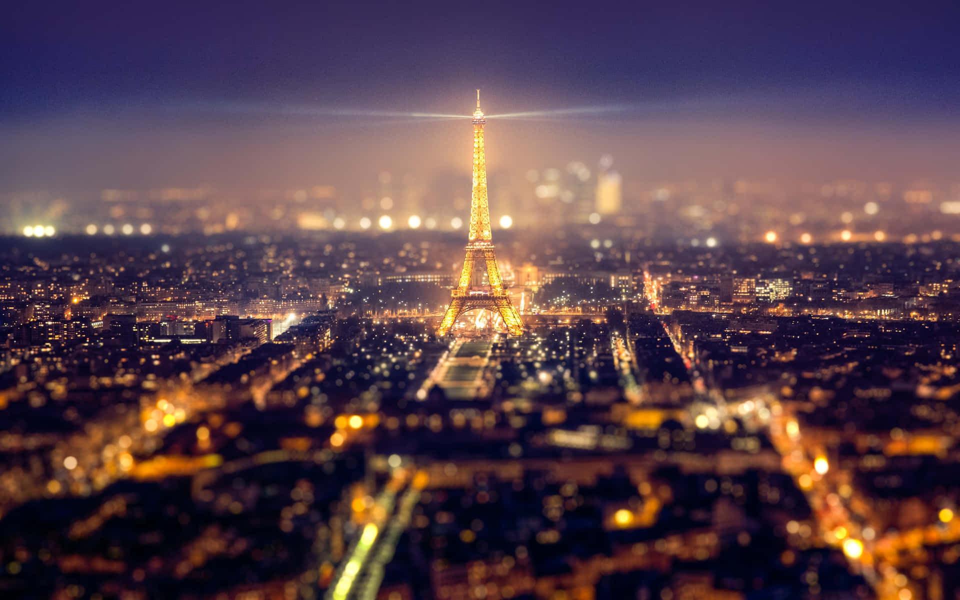 Eiffel Tower 桌布 壁紙 — 艾菲爾鐵塔在黑暗的天空中閃耀著金色光芒，下方是散景的城市燈光，呈現出令人驚嘆的夜景。