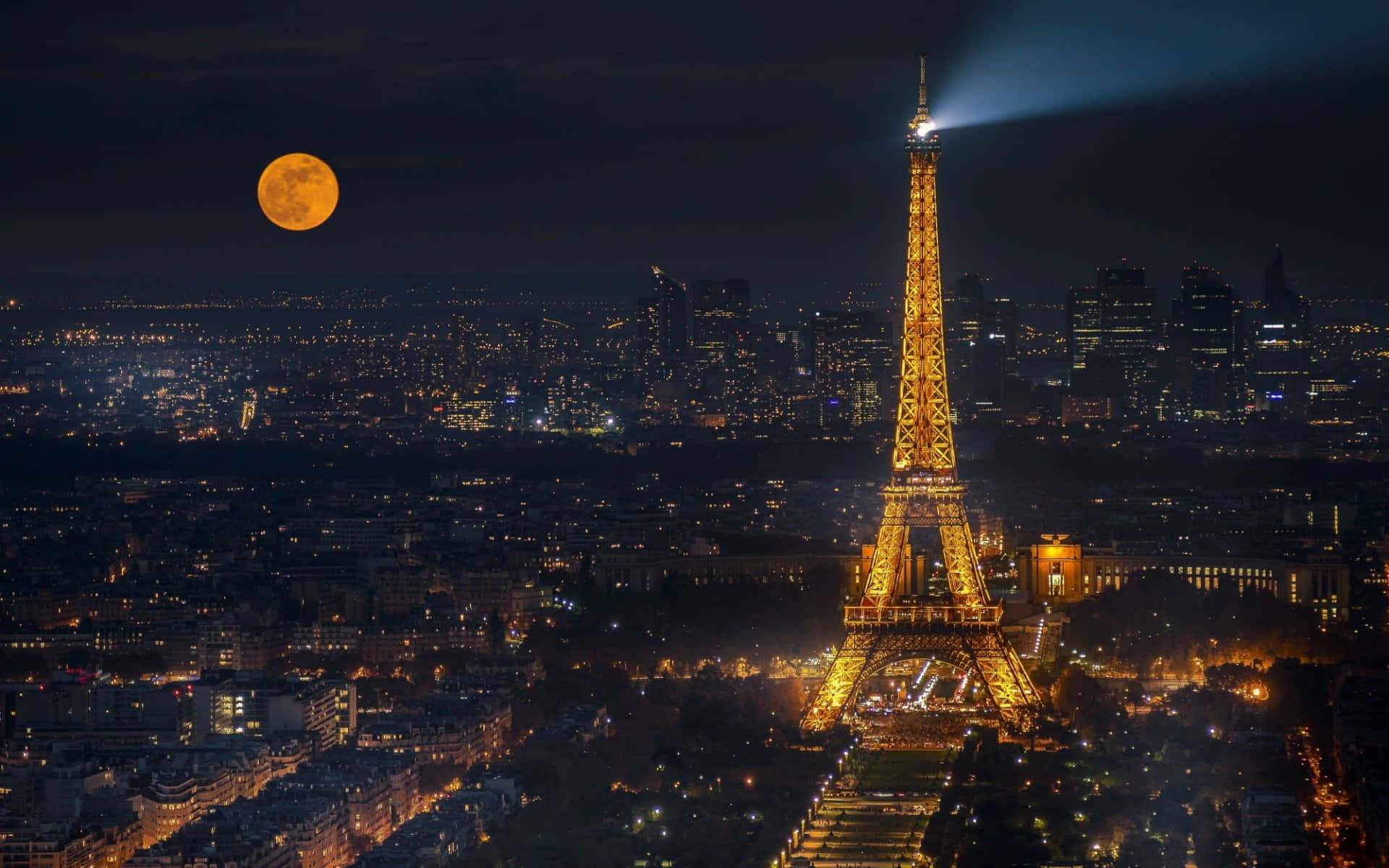 Eiffel Tower 桌布 壁紙 — 艾菲爾鐵塔在黑暗的天空中閃耀著金色光芒，滿月升起在巴黎屋頂和城市燈光之上。
