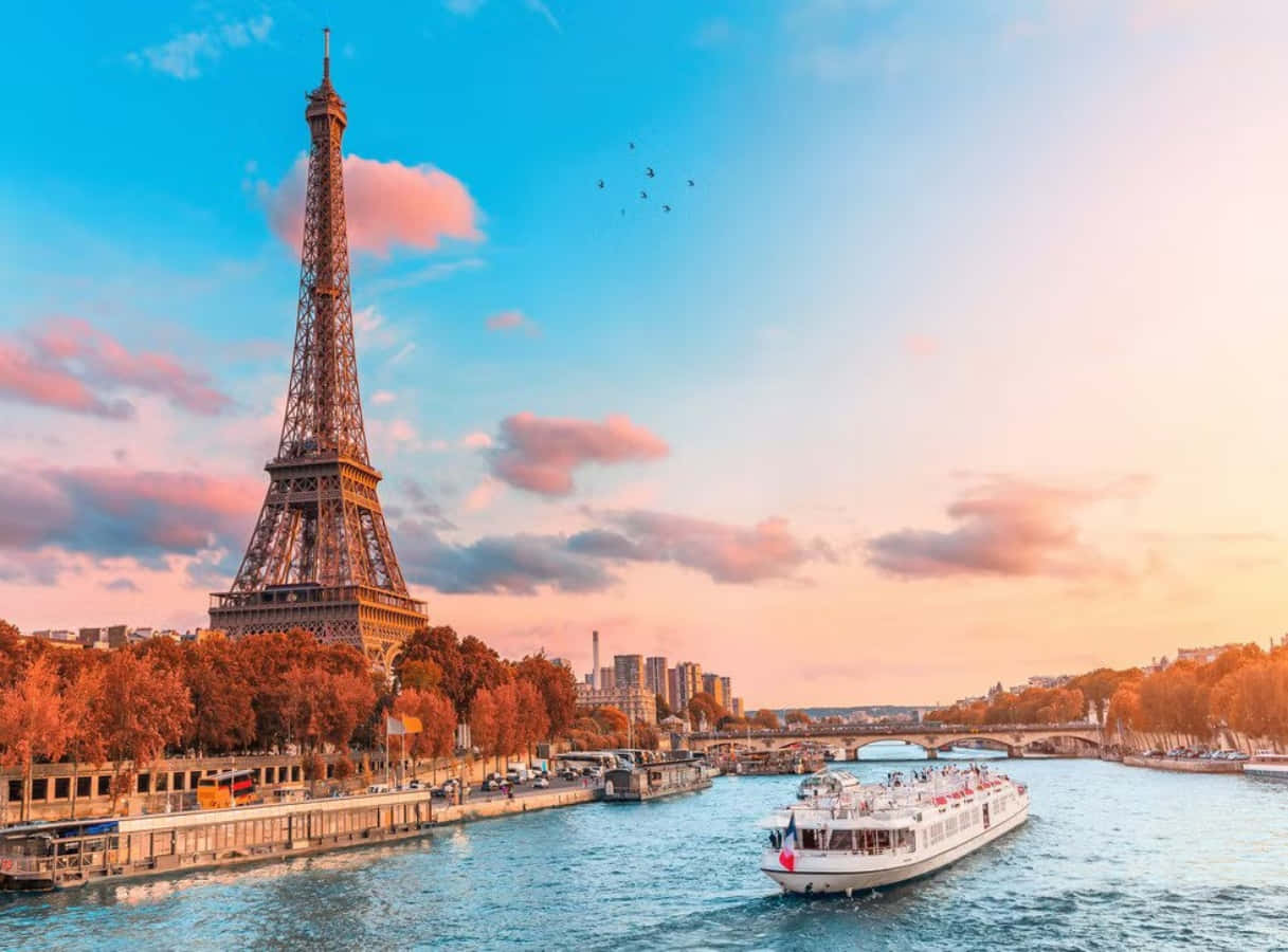 France 桌布 壁紙 — 艾菲爾鐵塔聳立在塞納河畔，夕陽下，一艘遊輪在色彩繽紛的秋樹下駛過。
