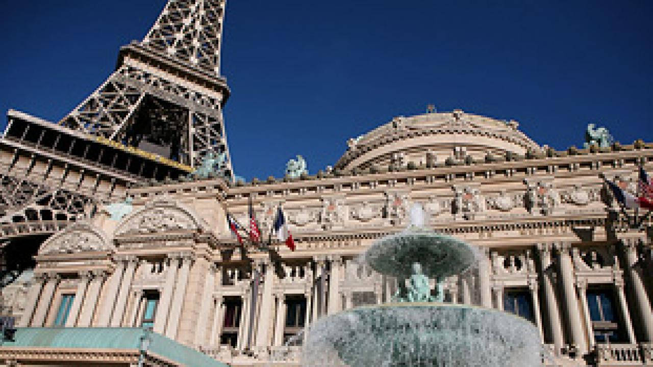 Paris Las Vegas 桌布 壁紙 — 艾菲爾鐵塔聳立於一座宏偉的新古典主義建築之上，建築前有噴泉在清澈的藍天下噴水。